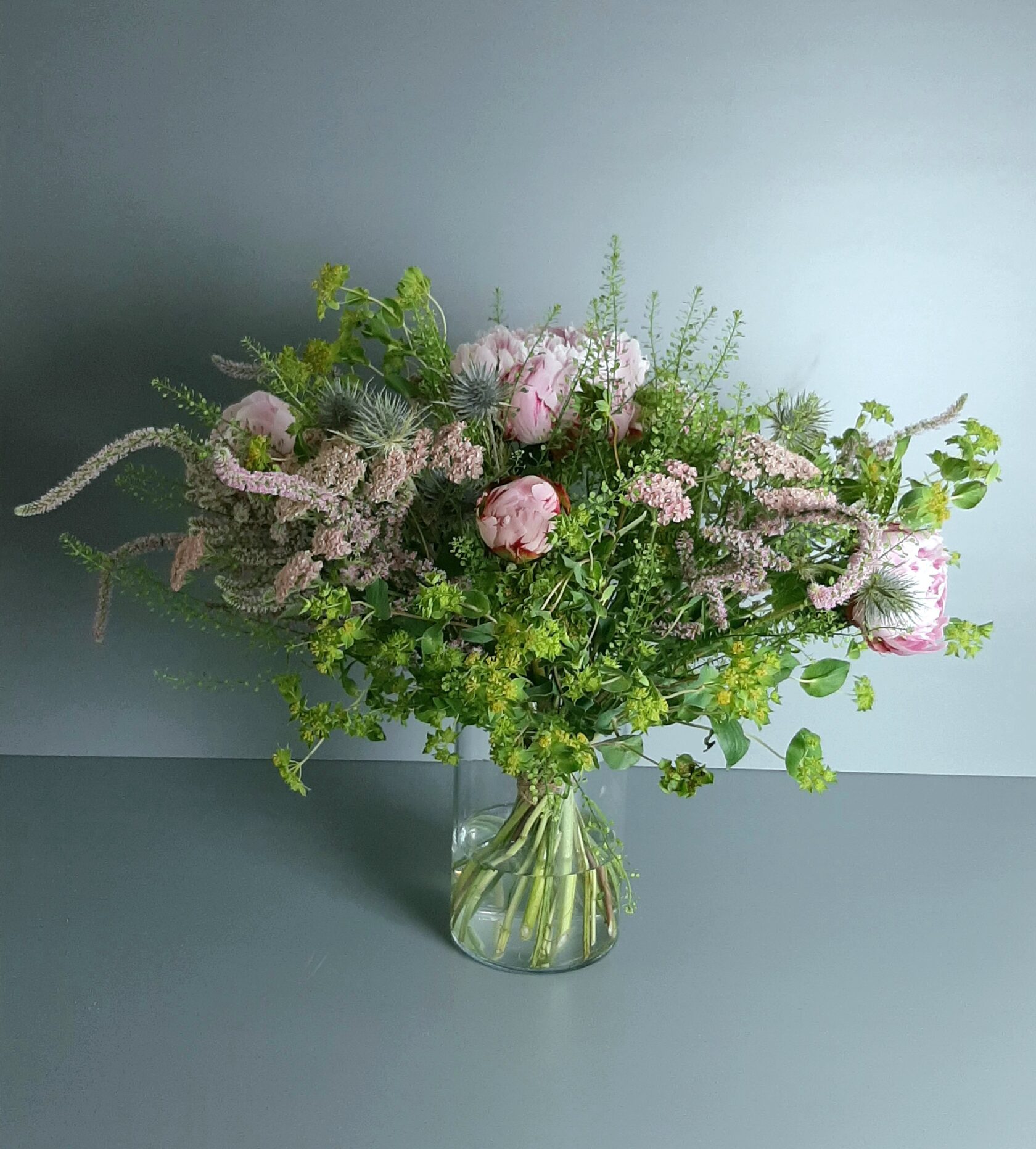 A delicate bouquet in a glass vase, harmoniously combining pink peonies, fluffy astilbe blossoms, greenery, and small decorative elements.