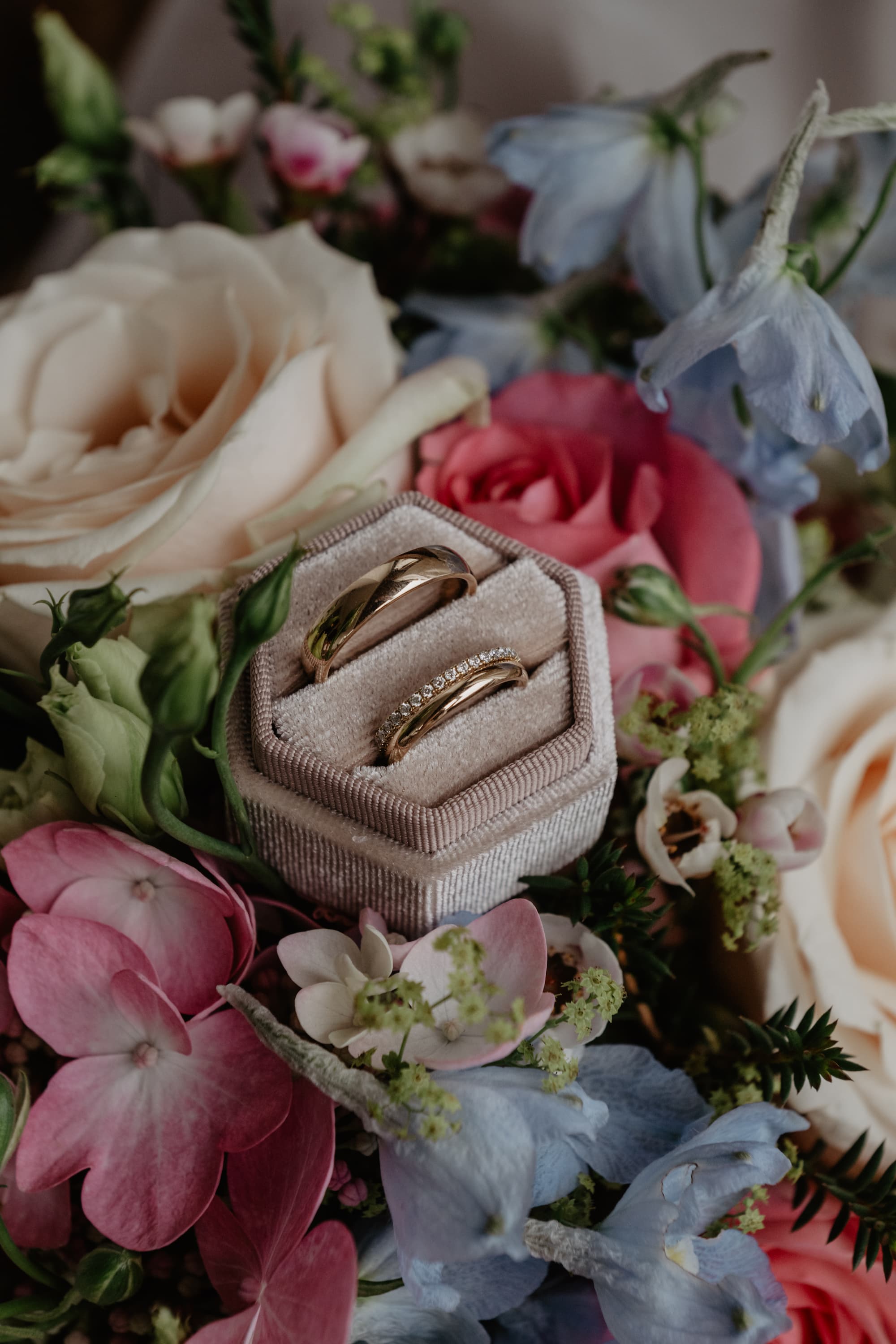 Close-up of wedding rings in a velvet ring box nestled among colorful bouquet flowers