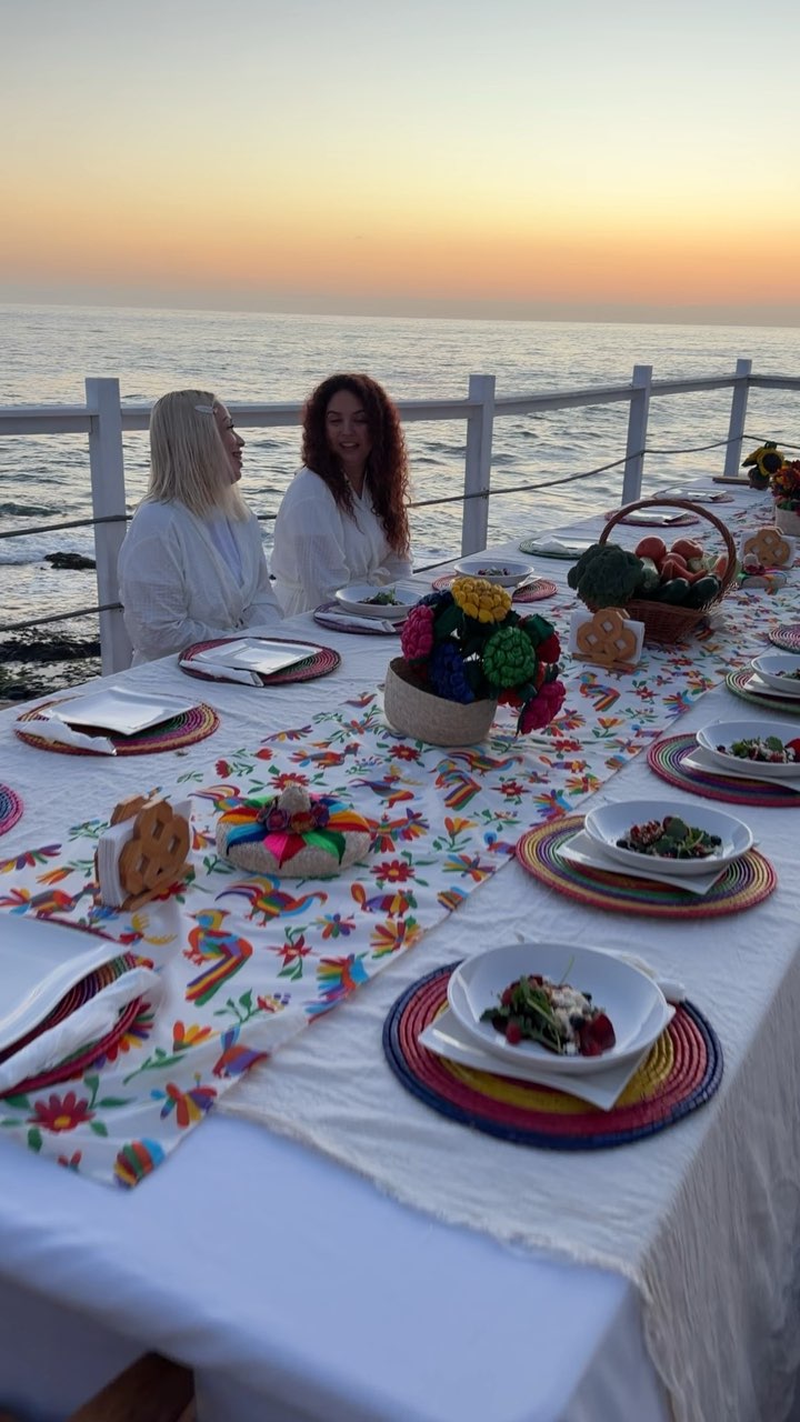 Una mesa larga de invitados en bata al atardecer, frente al mar