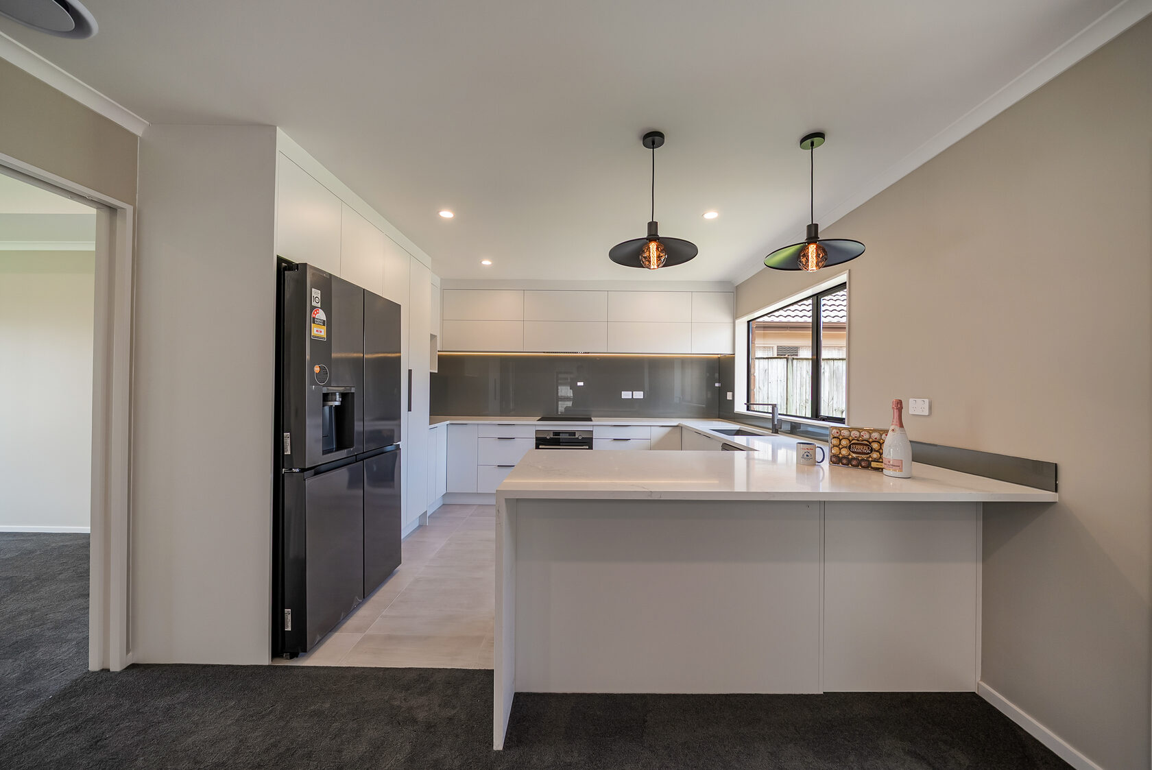 Renovated Flat Bush kitchen with white cabinetry, grey splashback, peninsula bench and black pendant lights