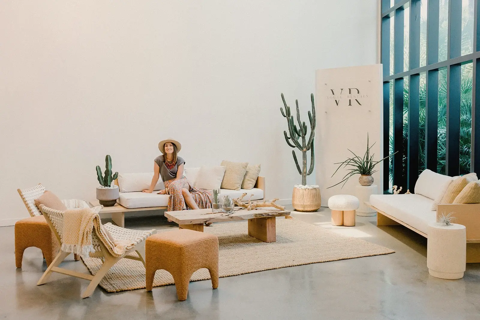 Katya Gustova, founder of Plants for Friends, in a sun hat on a white sofa among tall cacti
