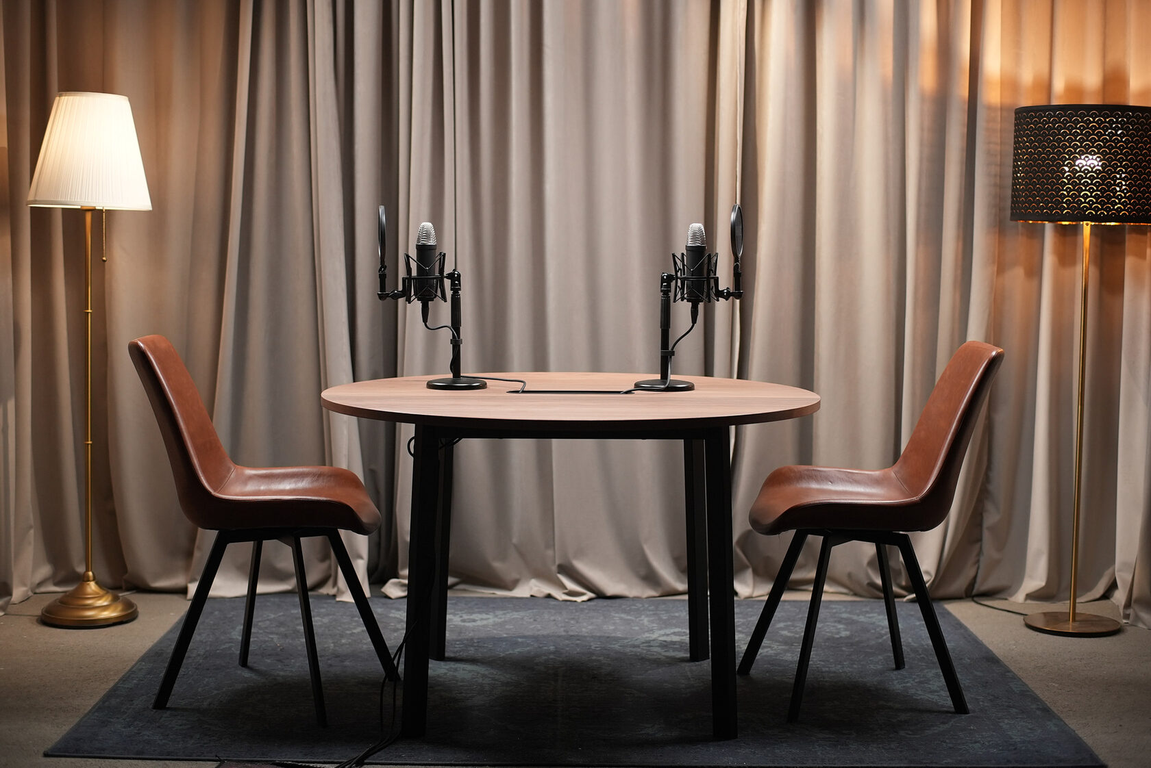 Стол, два кресла и два микрофона на фоне светлых штор между торшерами