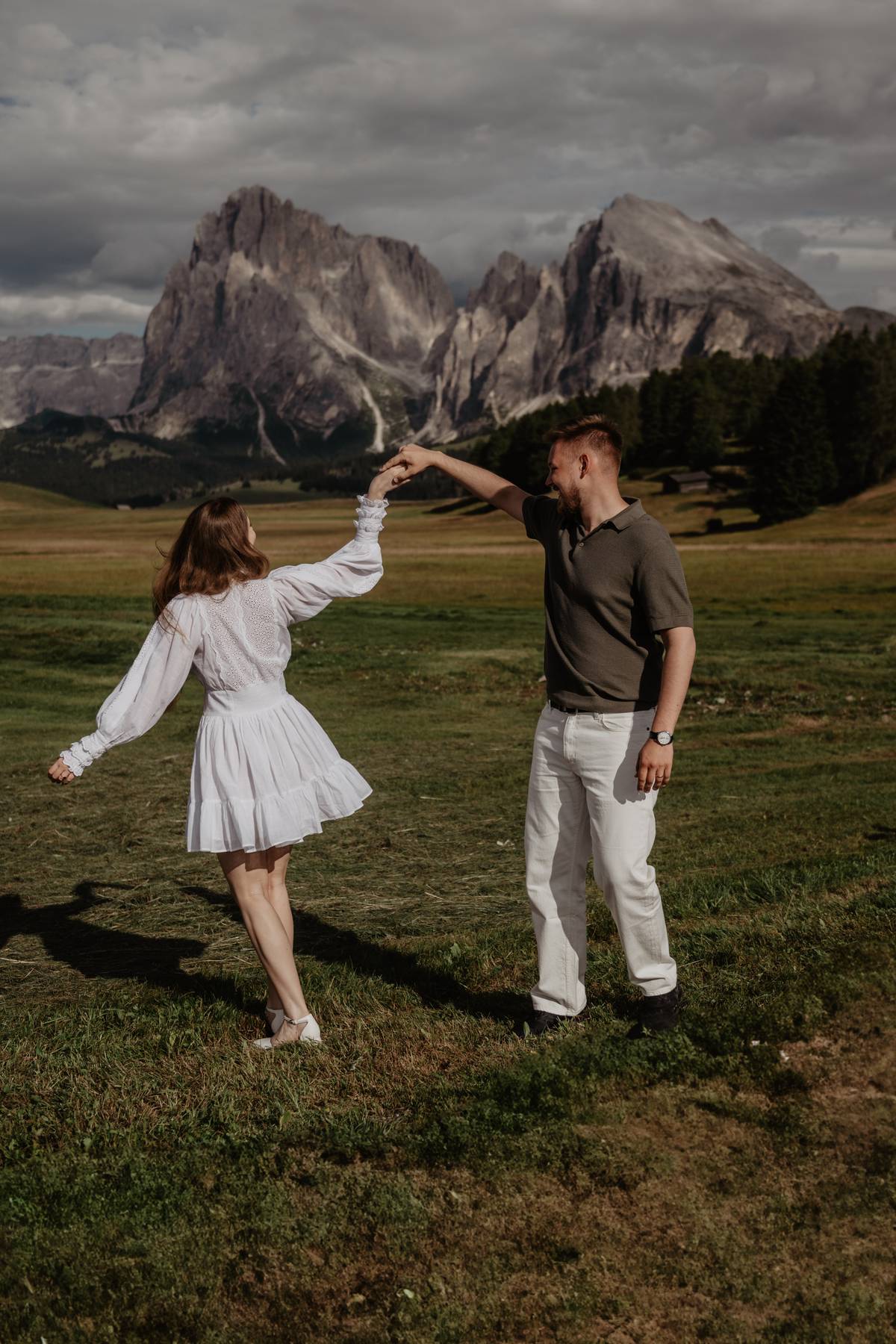 Engagement couple twirling in a meadow with dramatic Dolomites peaks behind, Italy, playful mountain session