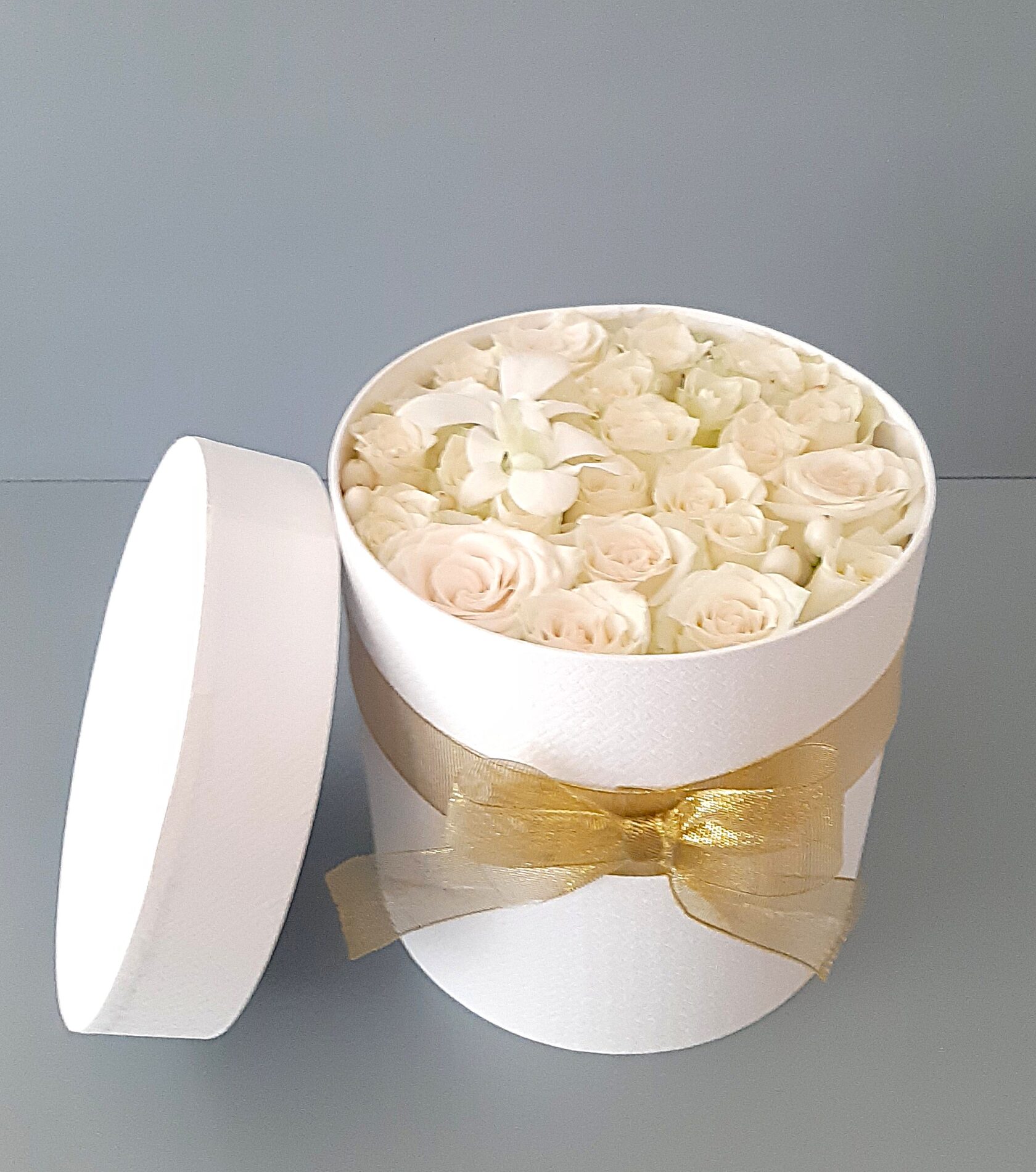 A floral arrangement of white roses in a round hat box with a gold ribbon.