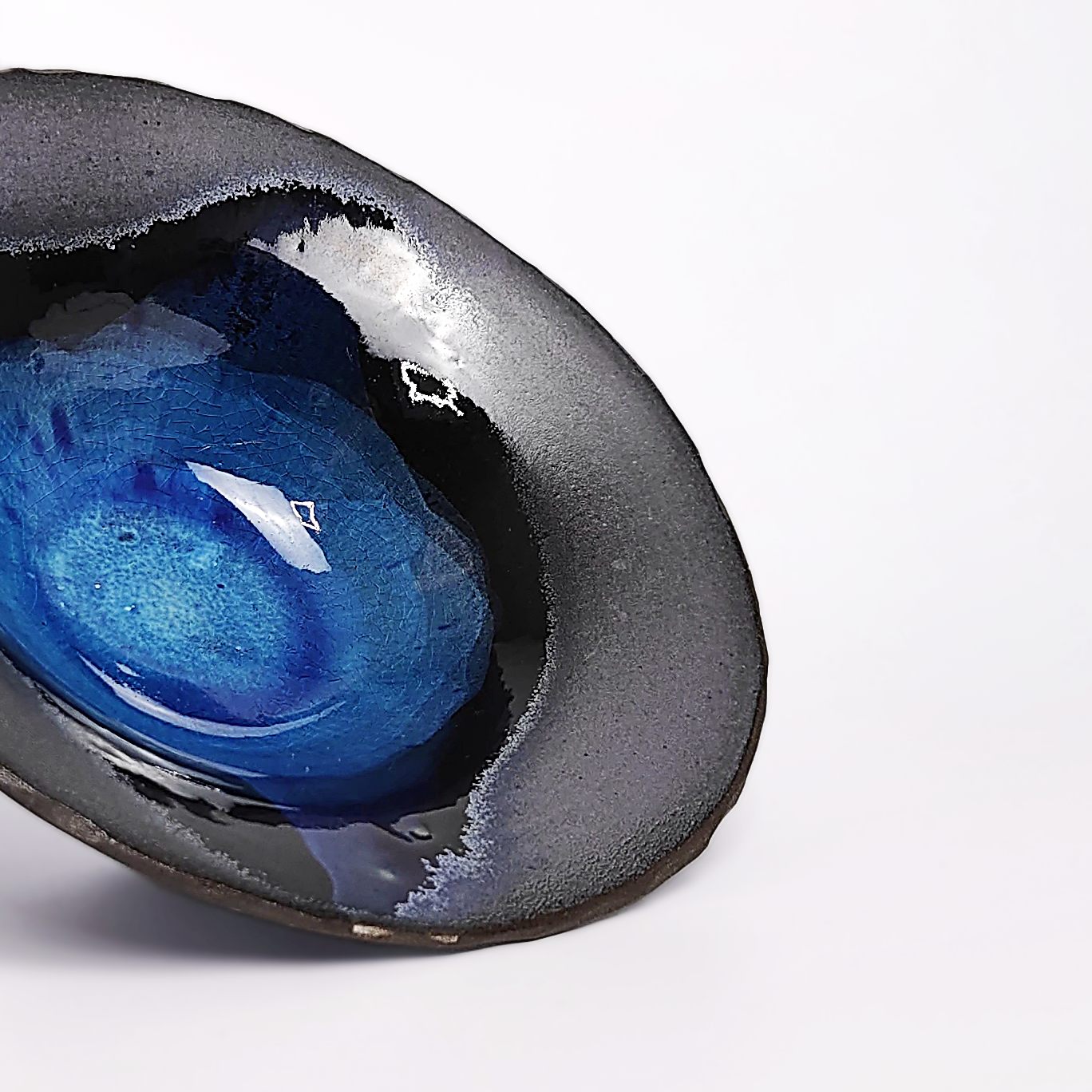 Handmade decorative ceramic plate with deep blue glossy glaze and black clay base