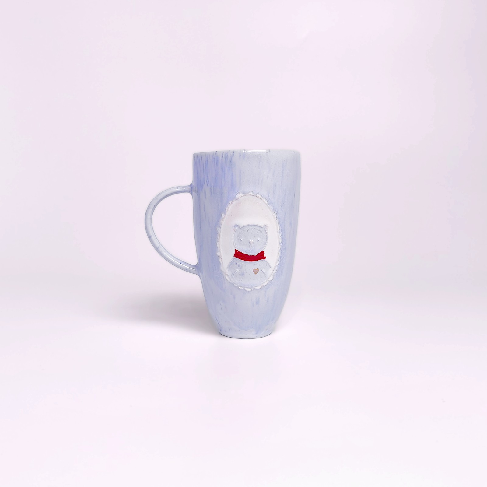 Unique handmade light blue ceramic mug with a pastel glaze, adorned with a sculpted medallion of a cute bear in a red scarf