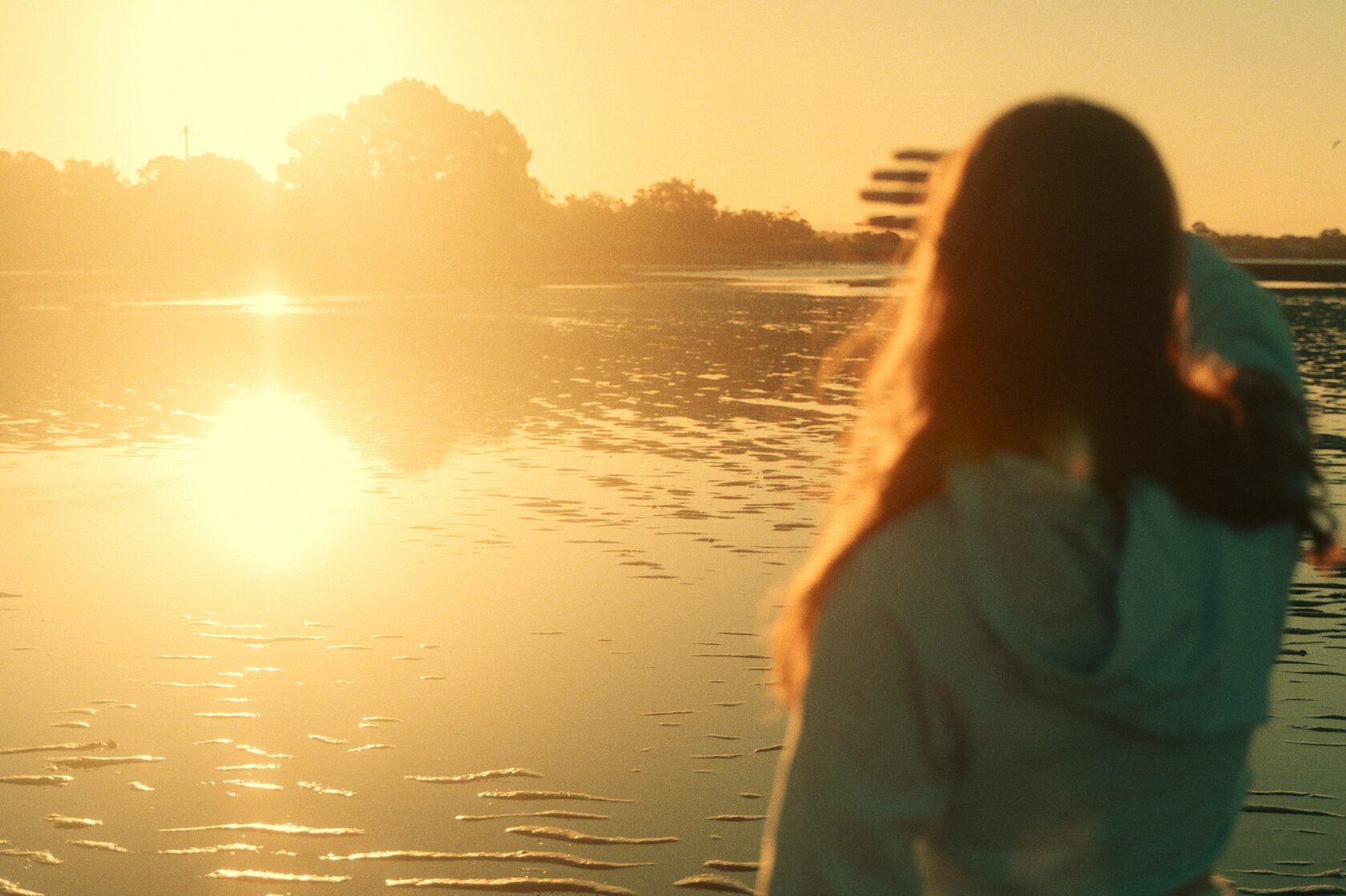 A woman seen from behind walking on a beach at golden hour