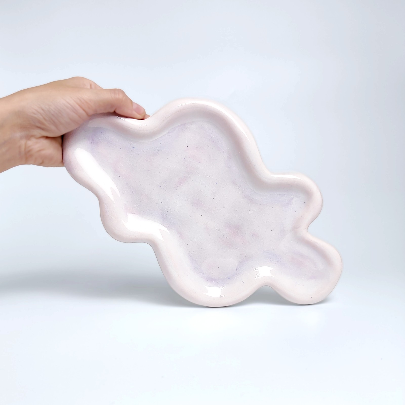 Unique handmade ceramic plate shaped like a cloud, featuring soft pastel pink glazing and an organic sculptural form