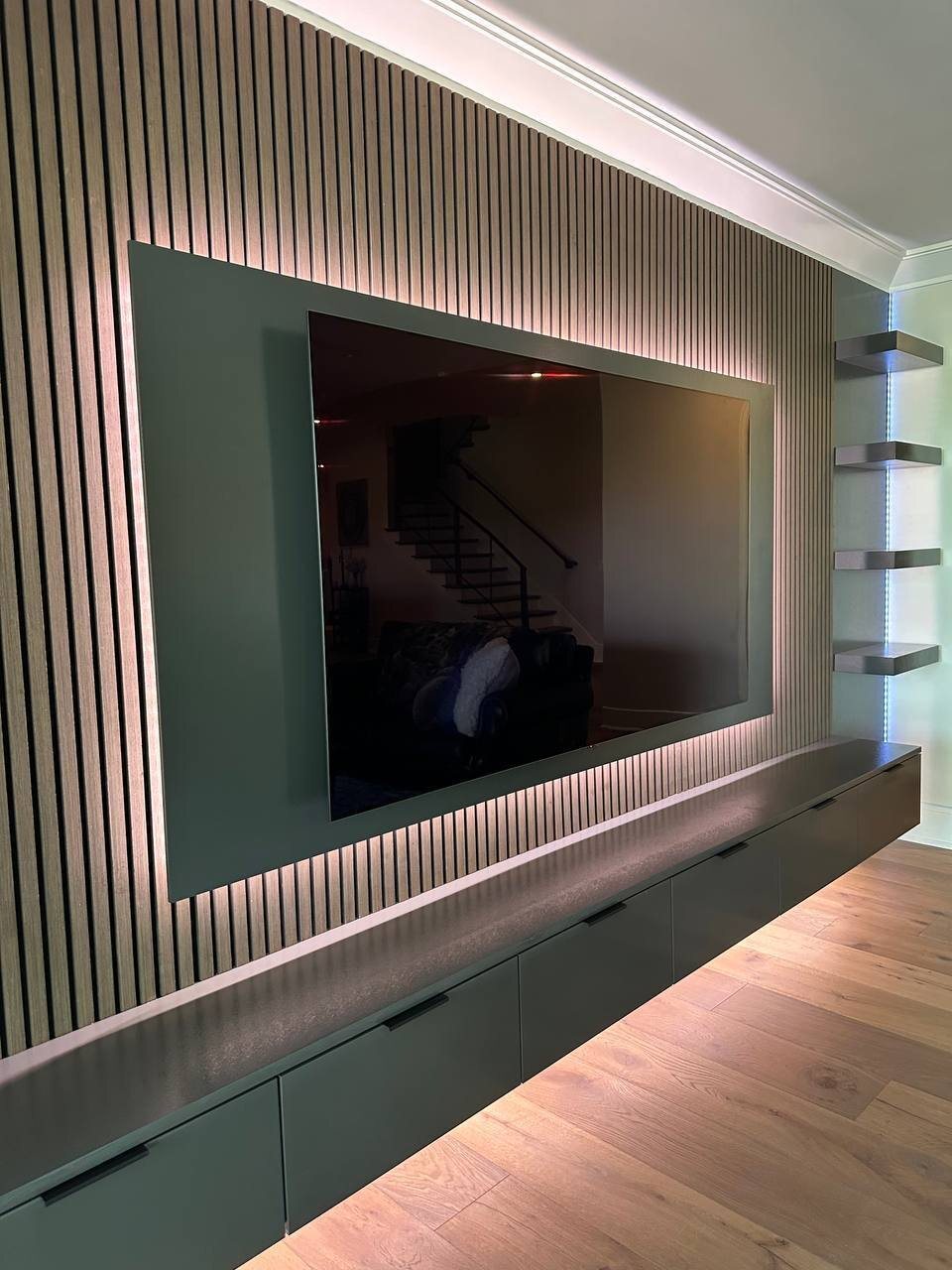 Wood slat accent wall with LED backlit TV panel and floating shelves