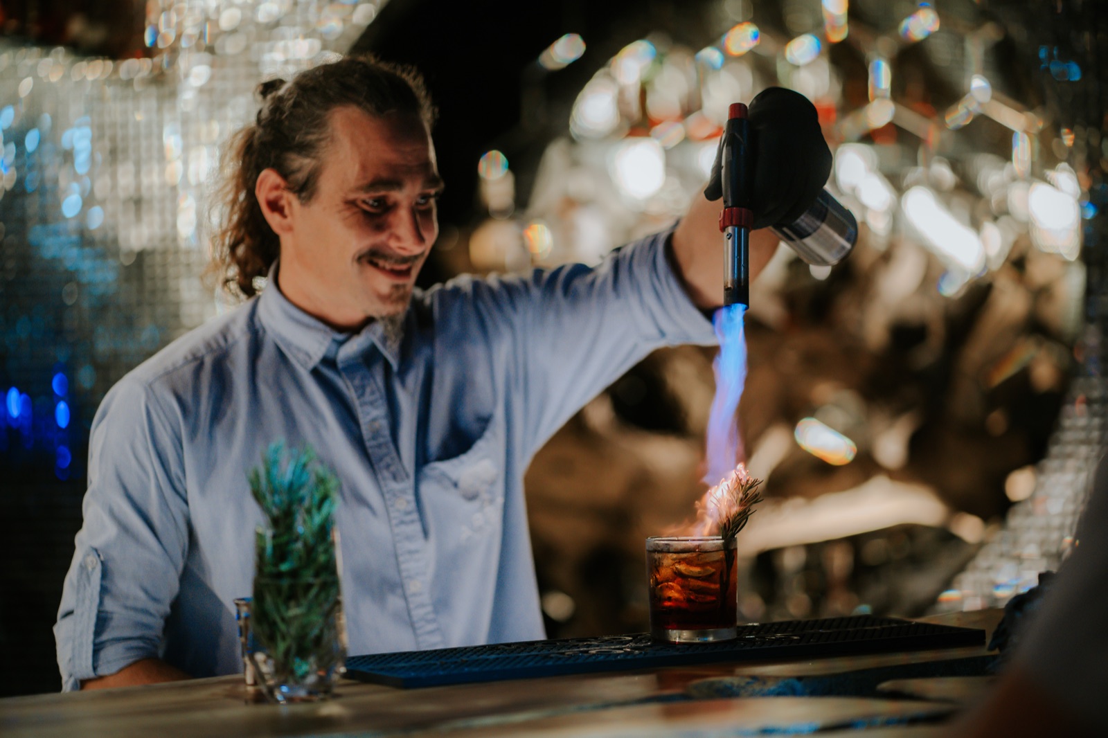 A Makanda bartender smiling as he torches a rosemary garnish on a cocktail