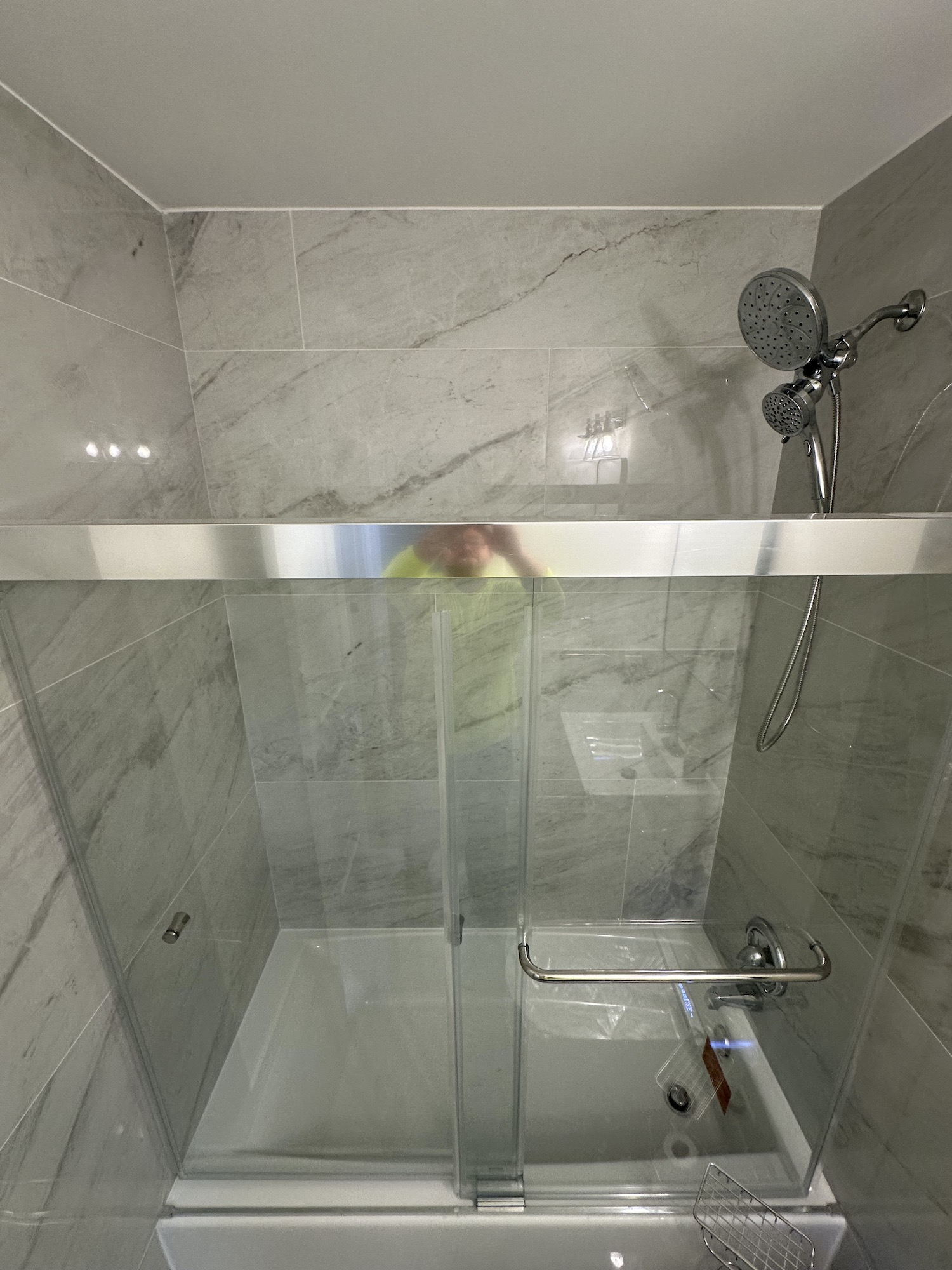New acrylic bathtub with sliding glass shower panel and large-format tile installed to the ceiling
