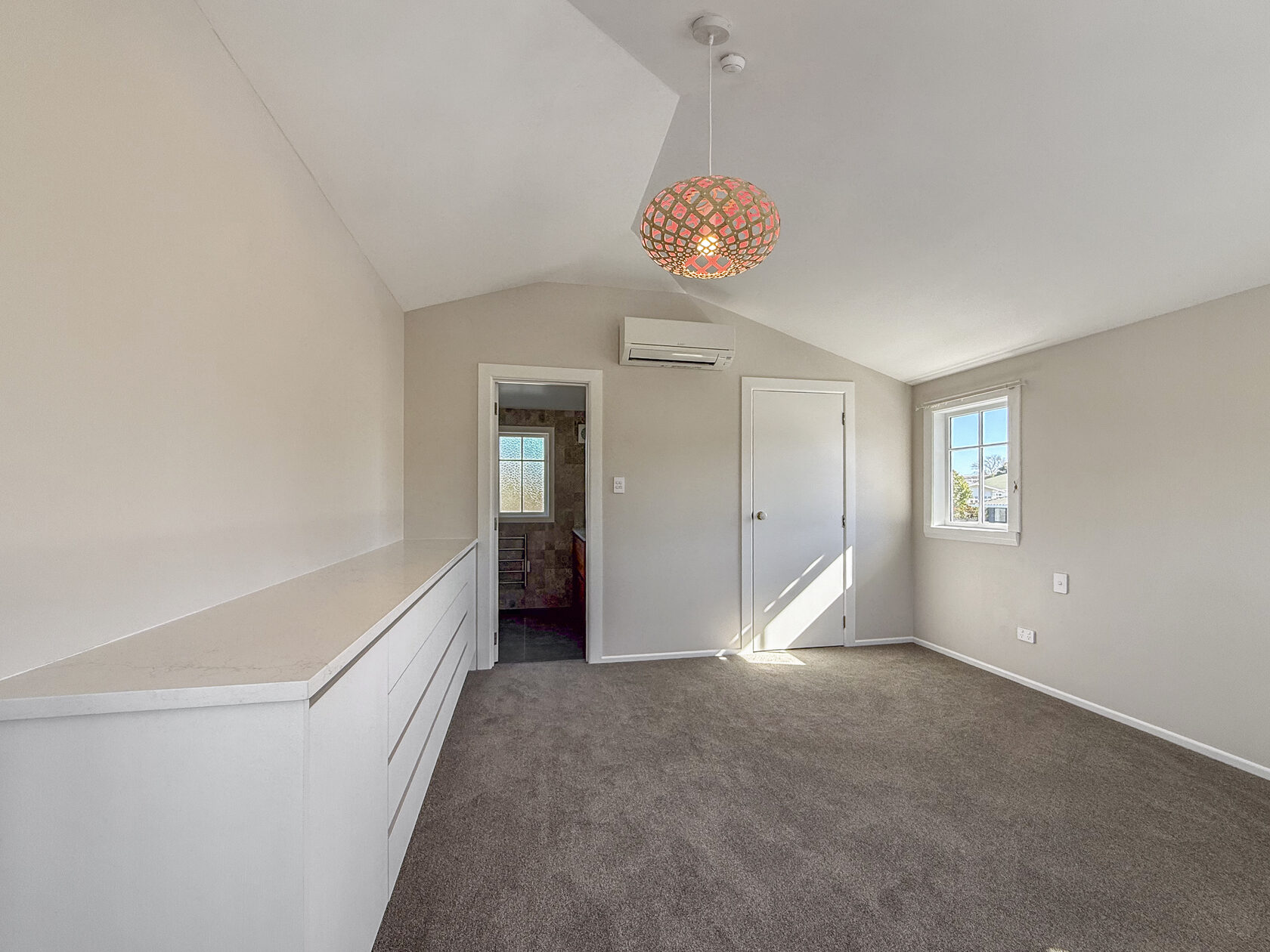 Carpeted bedroom with built-in white drawers, window and pendant light