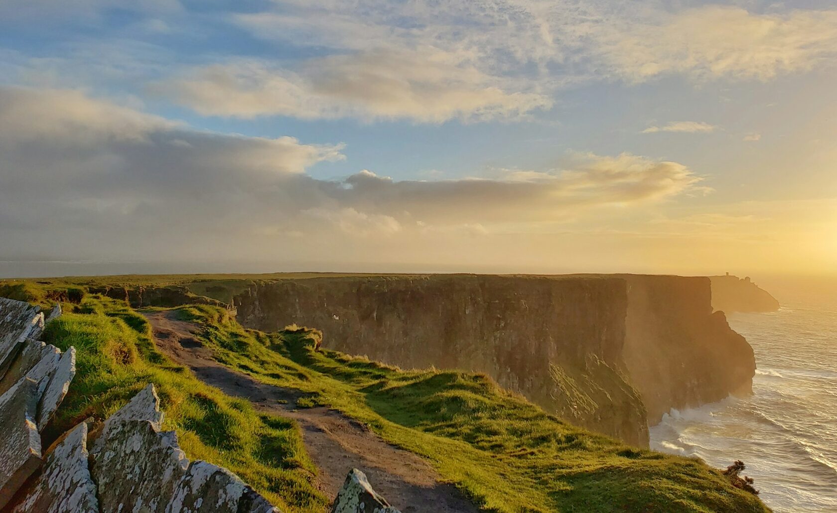 A small group of walkers on a green clifftop path along the Wild Atlantic Way, the sea sparkling far below on a bright day.