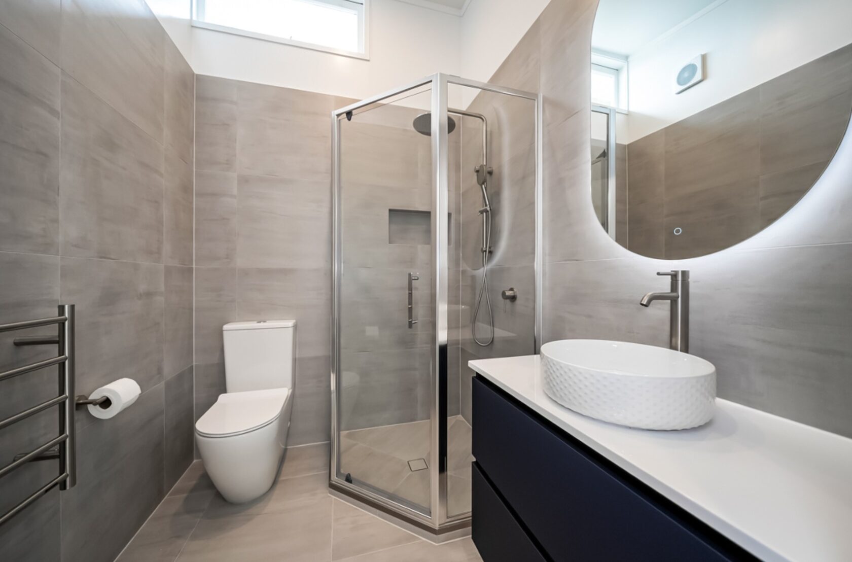 After: Hillcrest bathroom with glass shower, wall-hung vanity, round mirror and grey tiles