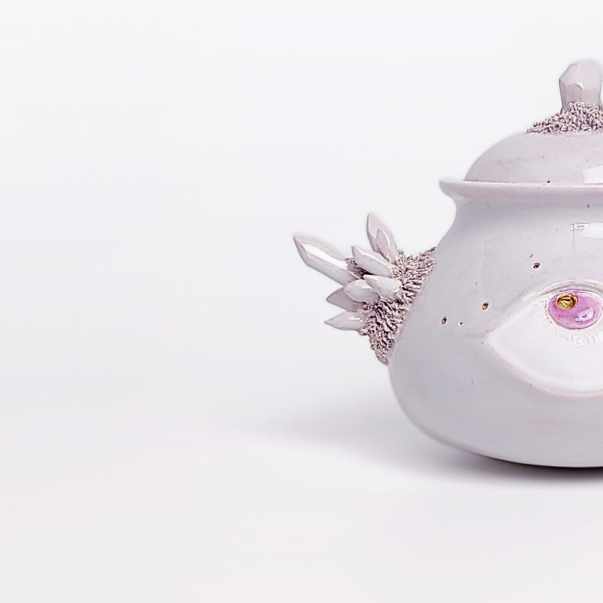 Unique handmade ceramic jar with a sculpted eye, textured crystal-like side elements, and soft pearlescent glaze