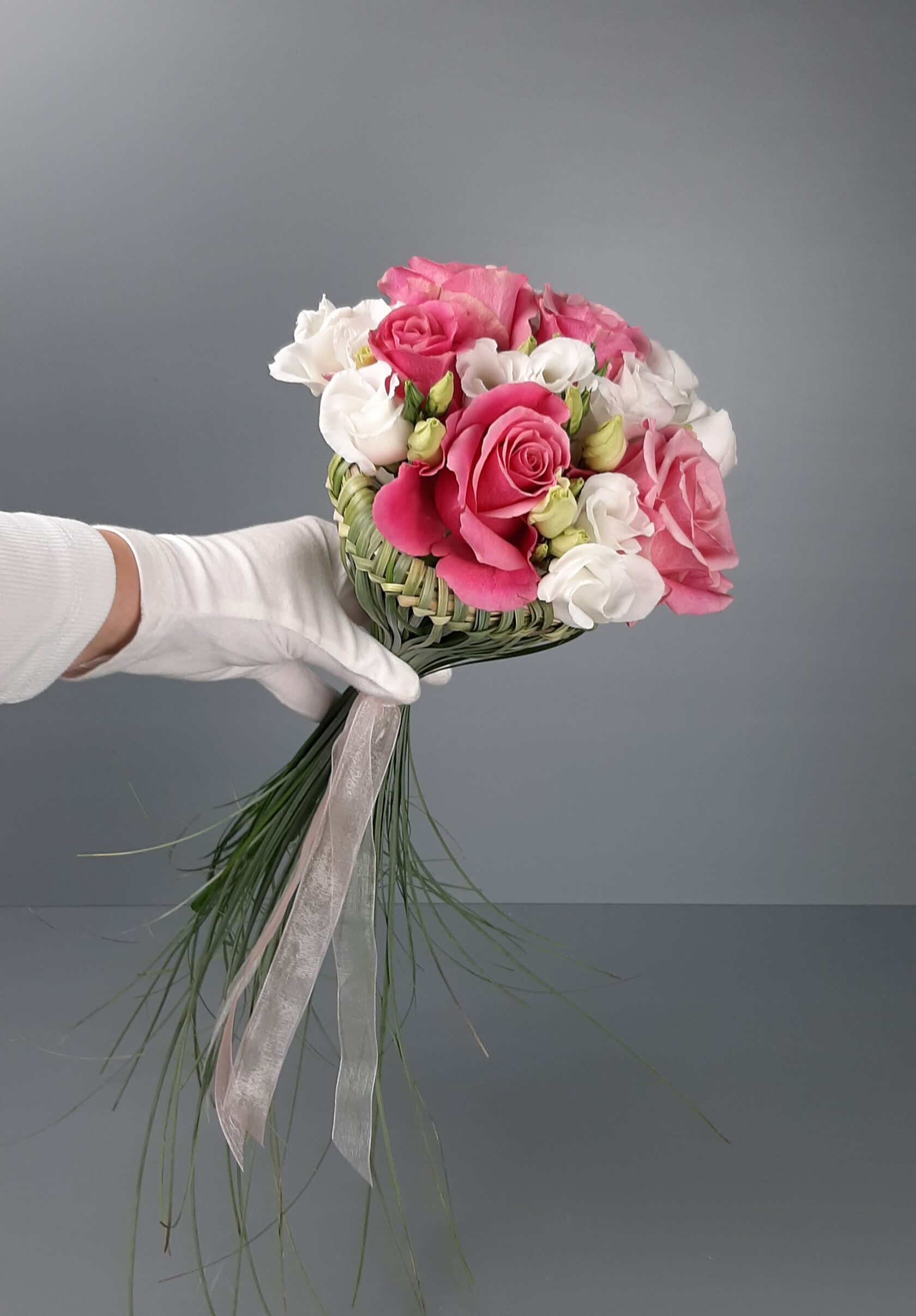 A bridal bouquet in pink and white tones, featuring a unique structural design made of greenery and long, cascading stems.