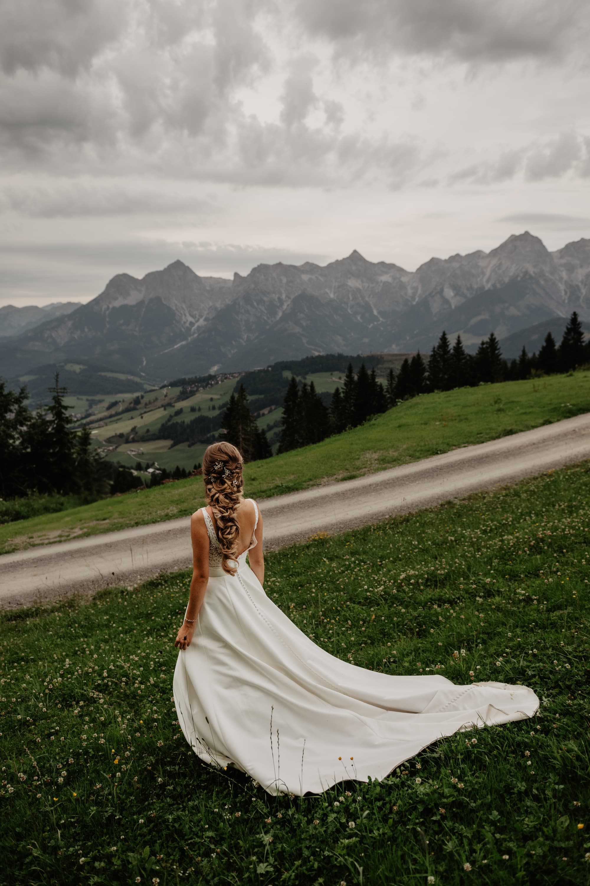 Bride with a long train looking toward alpine peaks in Austria, mountain wedding portrait