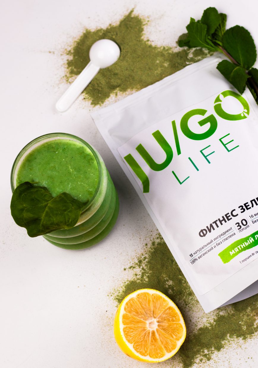 Упаковка JU/GO Life Фитнес зелень рядом со стаканом зелёного коктейля, мятой и лимоном