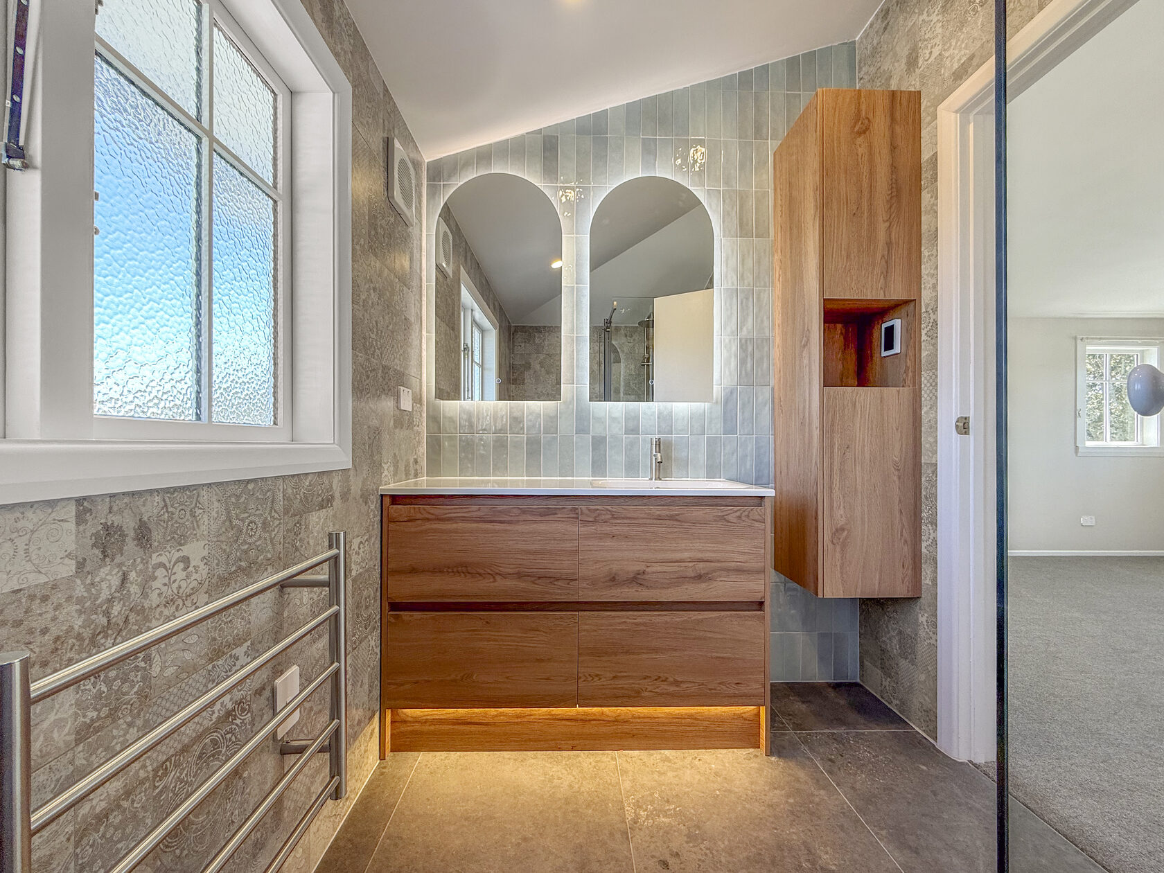 Timber bathroom vanity below twin arched mirrors and pale blue wall tiles