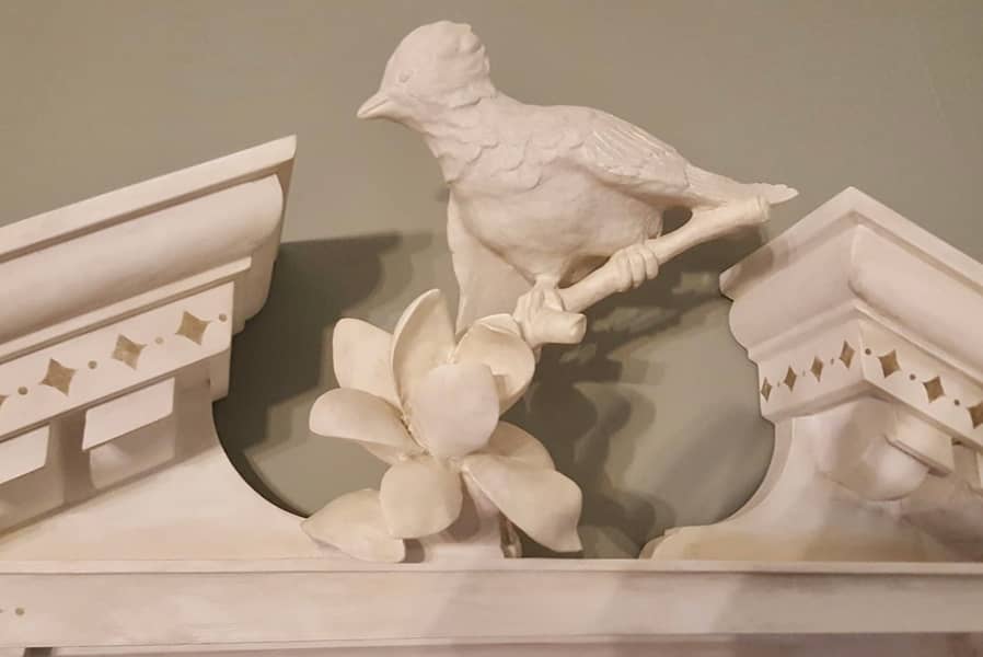 Detail of colonial style handcrafted mirror pediment with hand carved floral branch and bird on it