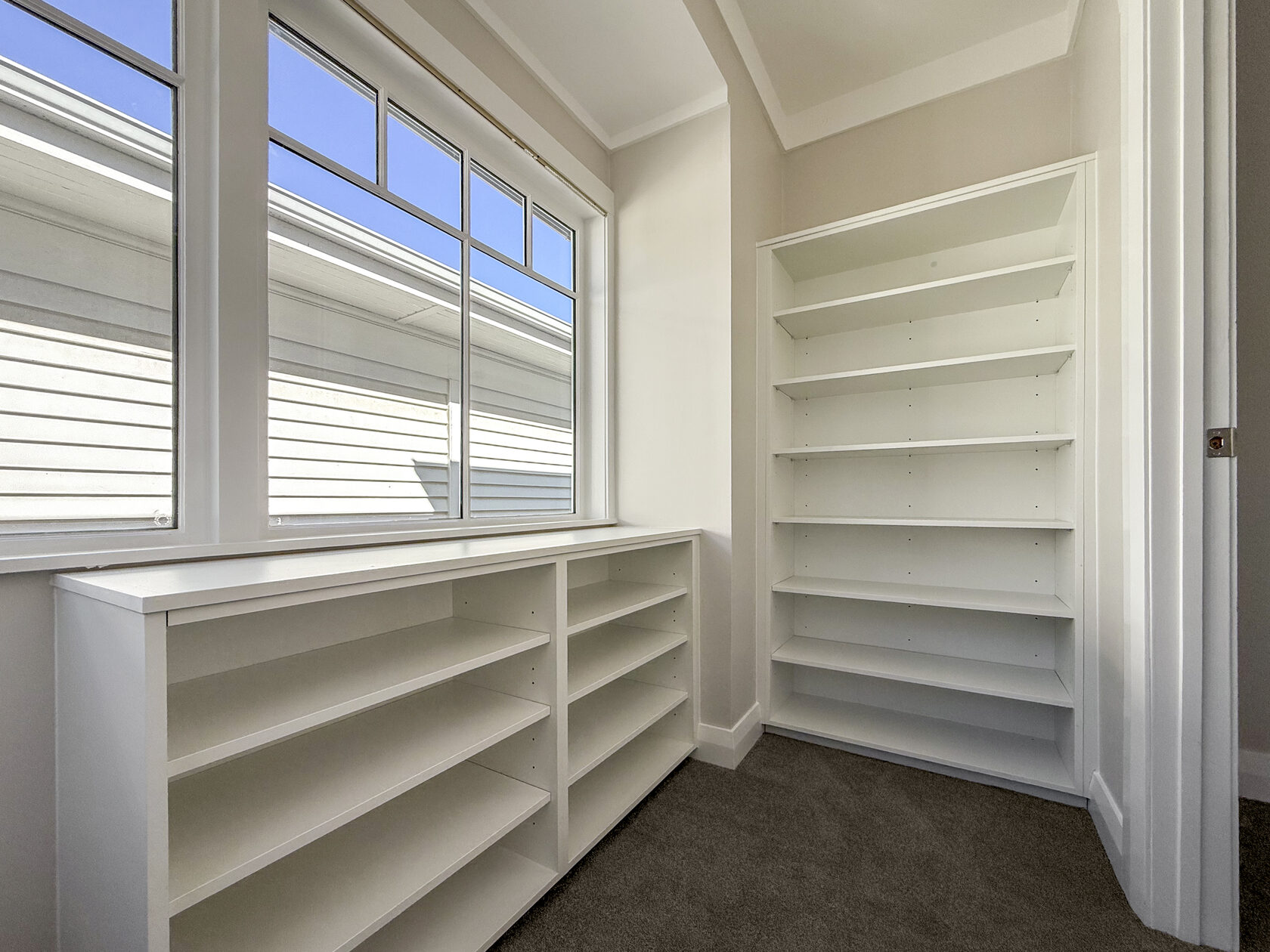Corner of a room with white built-in shelves beside tall windows