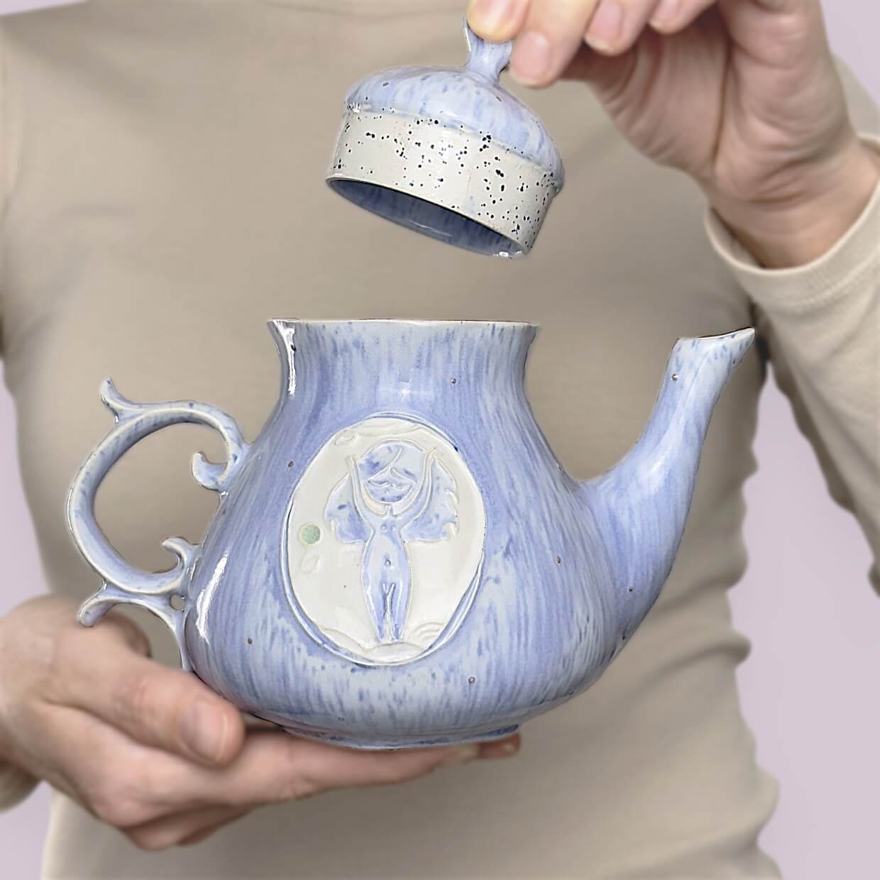 Handmade ceramic teapot from an original tea set, featuring a sculpted forest fairy on soft blue speckled glaze. Curved handle and removable lid. A whimsical and unique piece of functional art.