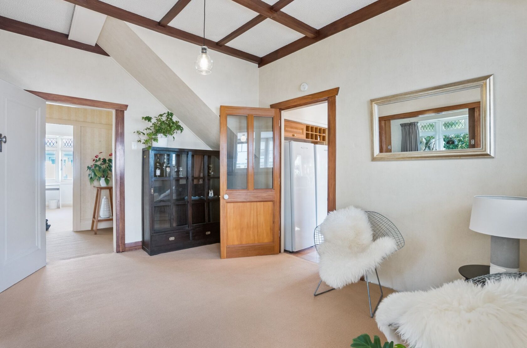Before renovation: carpeted room beneath the stairs with timber trim and a display cabinet