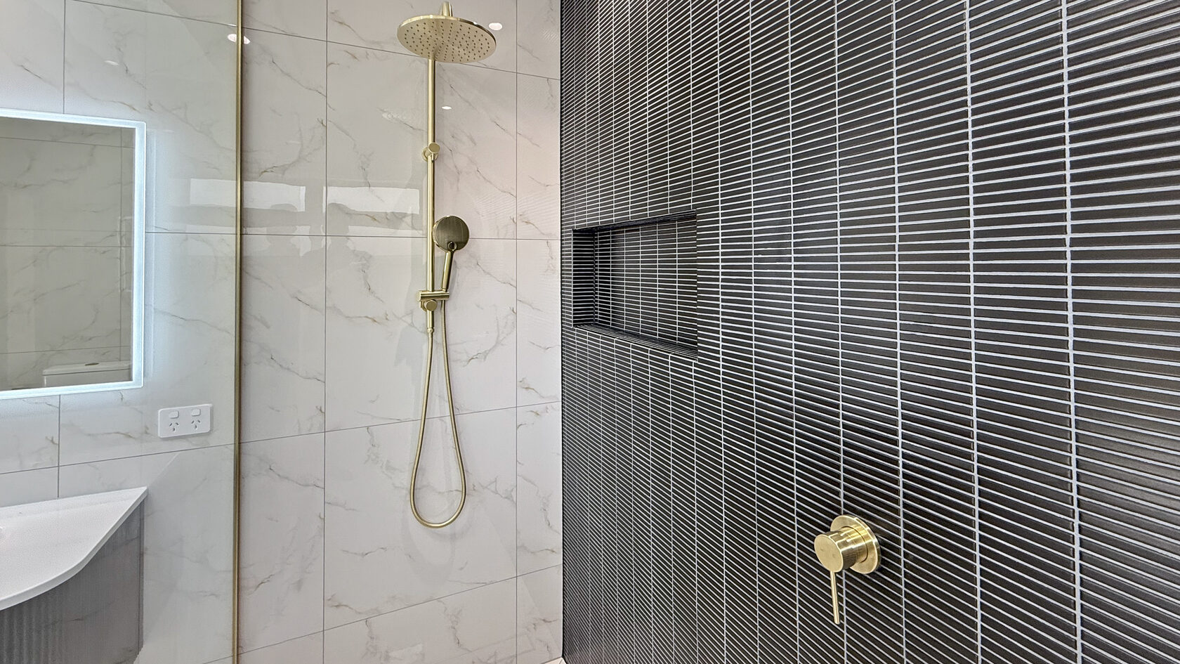 Walk-in shower with black feature tiles, marble-look walls and brass shower fittings in St Heliers.