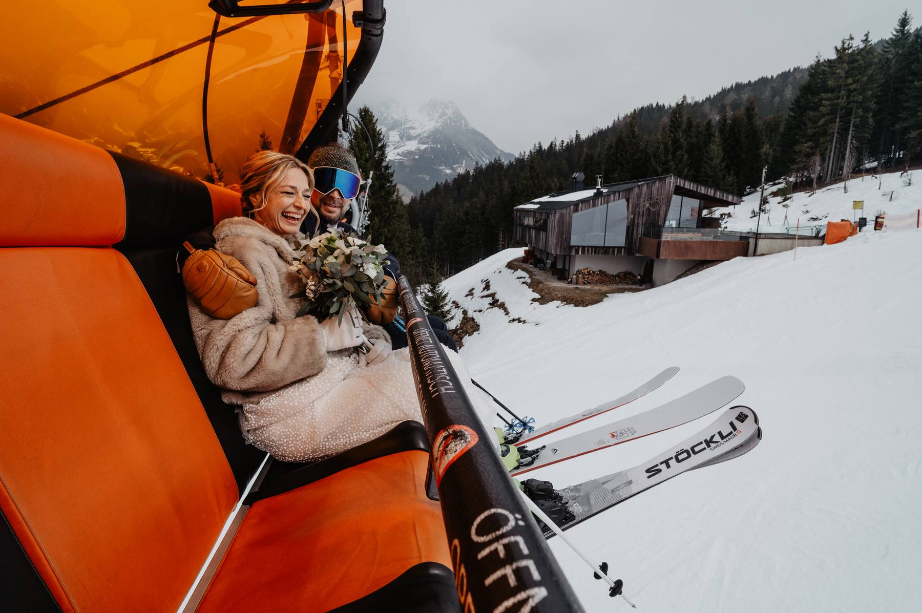 Smiling winter bride holding her wedding bouquet on a ski lift above snow-covered alpine slope