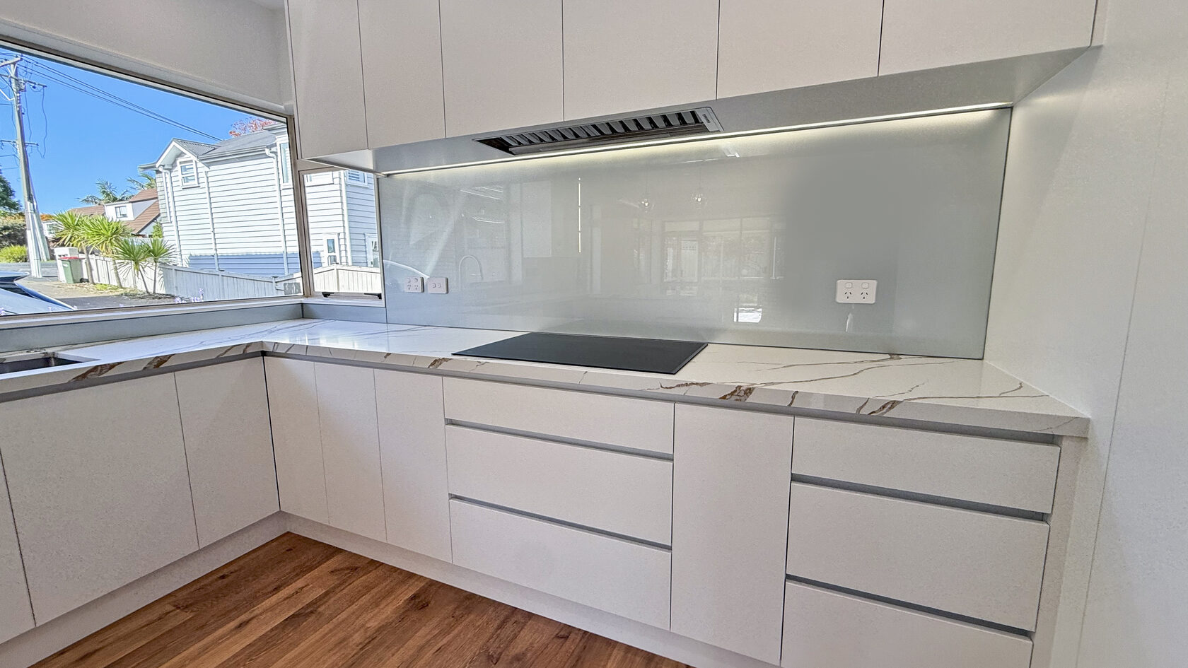White handleless cabinets, stone benchtops and glass splashback in a St Heliers kitchen.