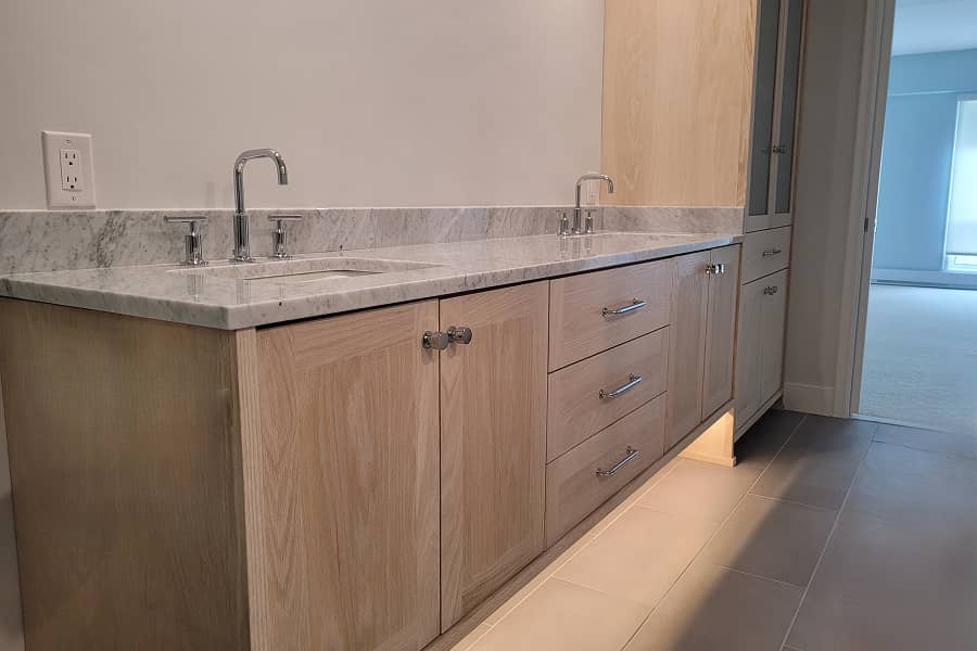 Custom bathroom vanity with double sinks, marble countertop and tall storage cabinet in pickled white oak and undercabinet lighting