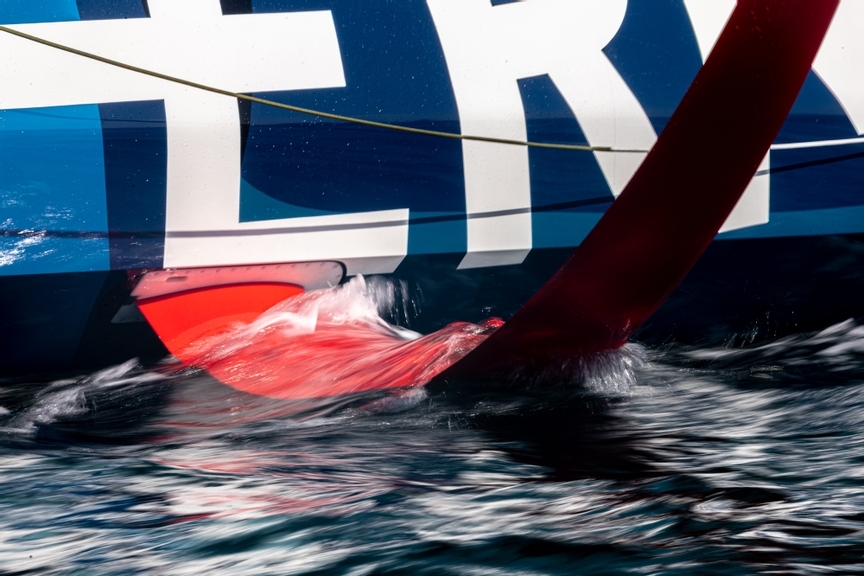 A close view of an IMOCA yacht’s foil and hull moving through the water