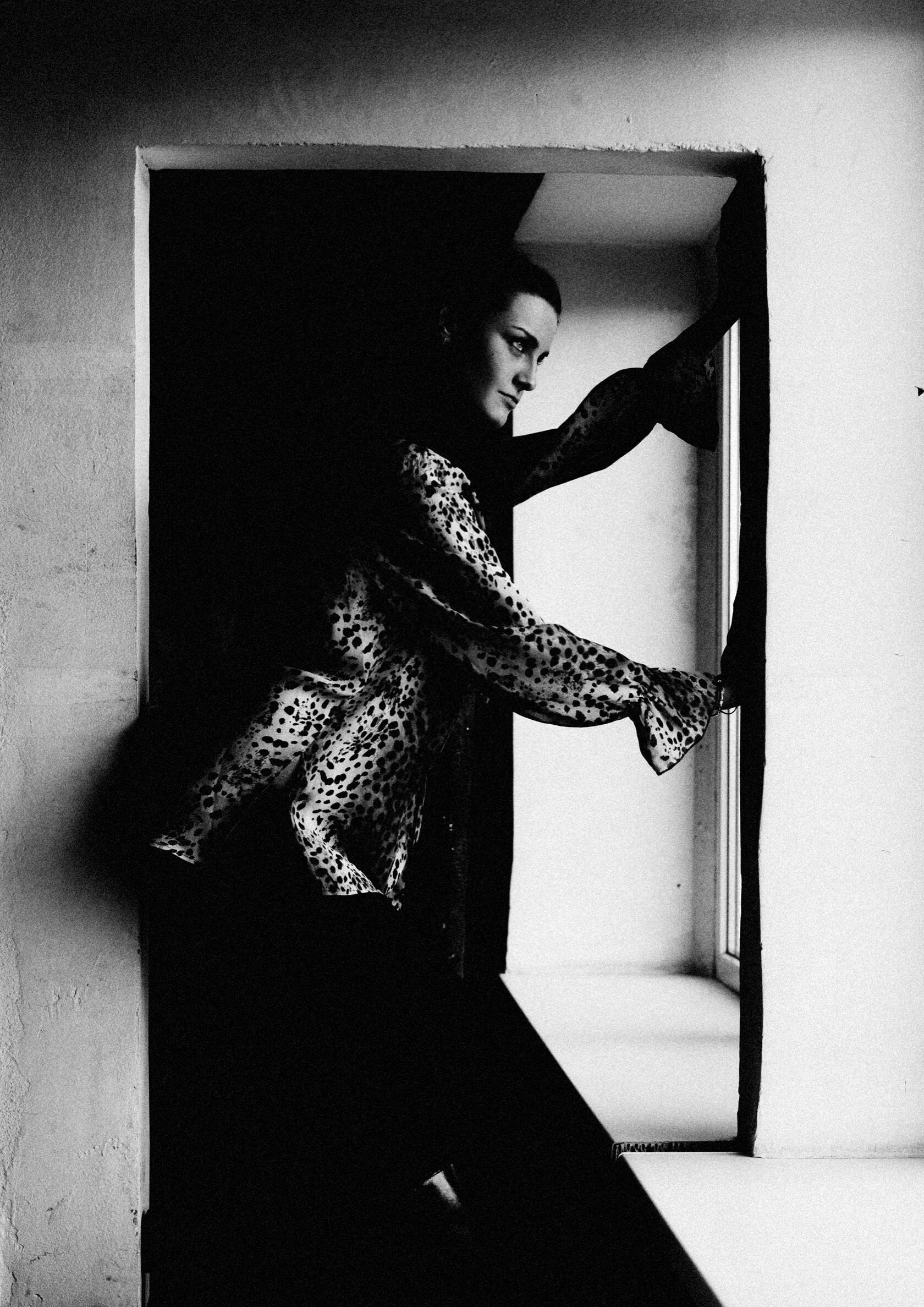 Schwarz-Weiß-Portrait einer Frau am Fenster mit gemustertem Oberteil
