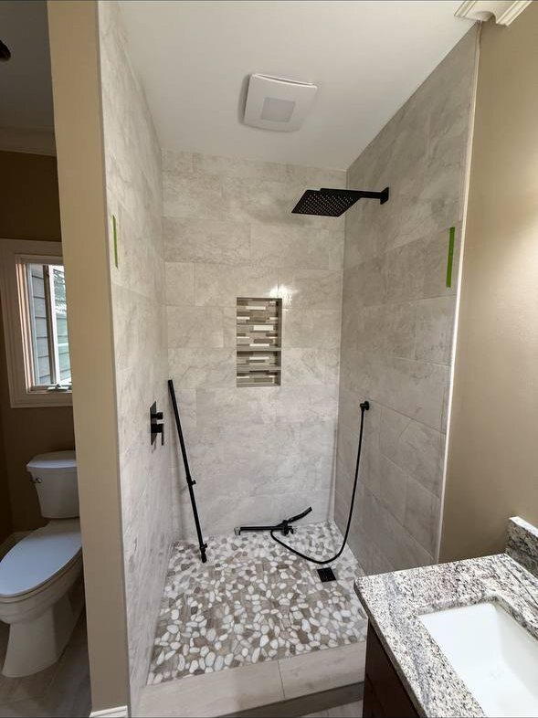 Walk-in shower remodel with pebble stone floor, tiled niche and matte black rain shower