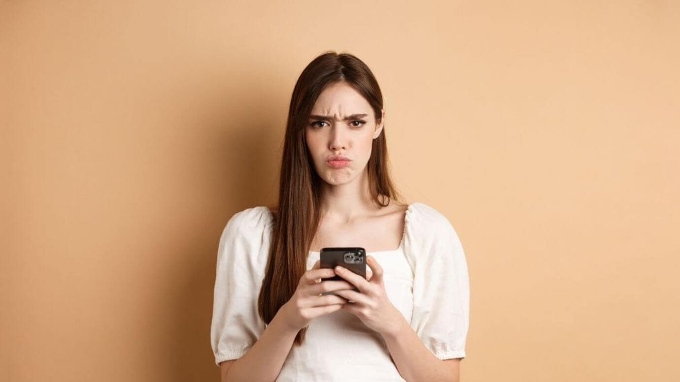 Upset beautiful brunette woman holding mobile phone with a displeased expression