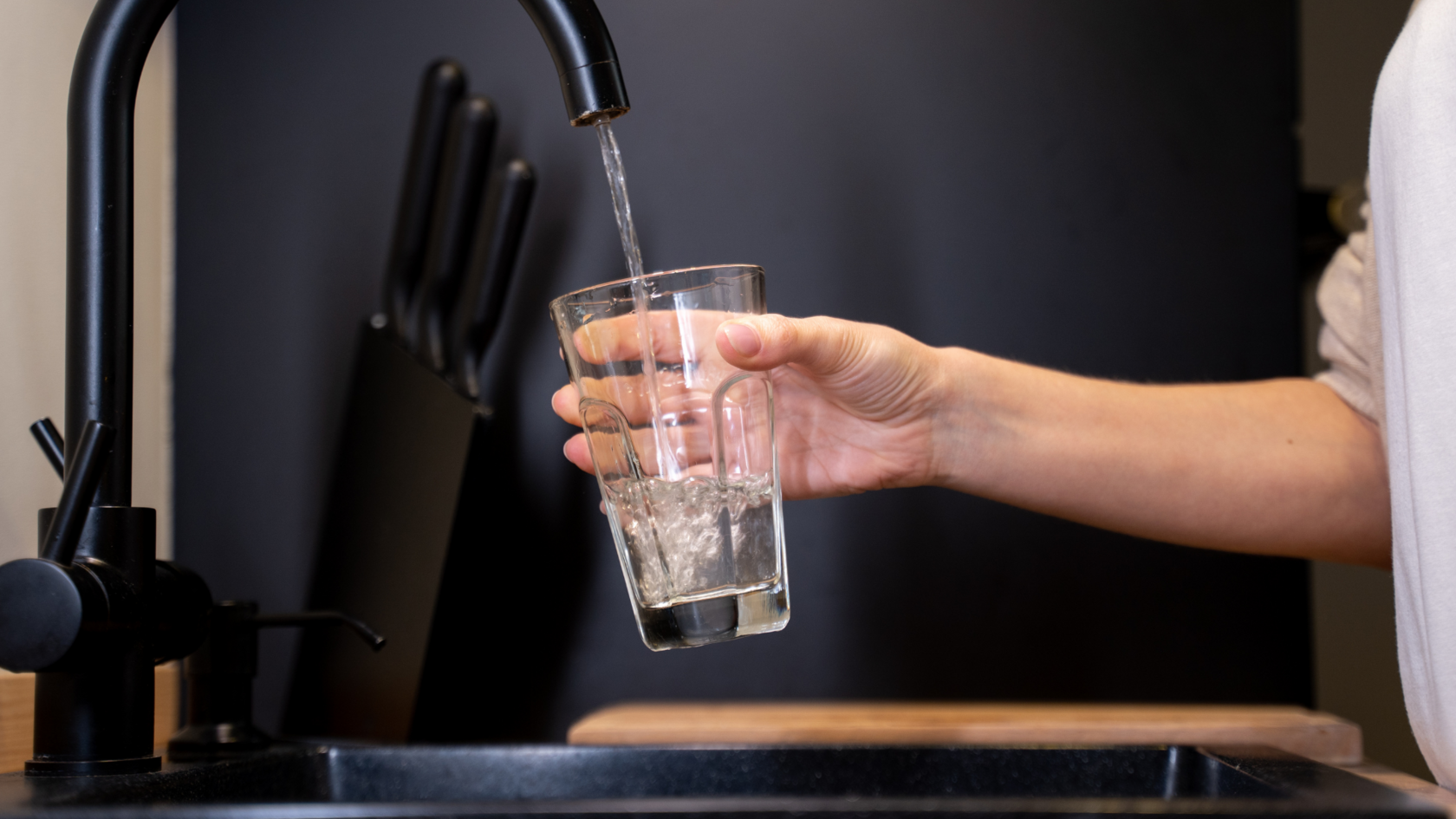 A person fills a glass with tap water from a modern black kitchen faucet, illustrating the question of tap water safety and drinkability in Cyprus