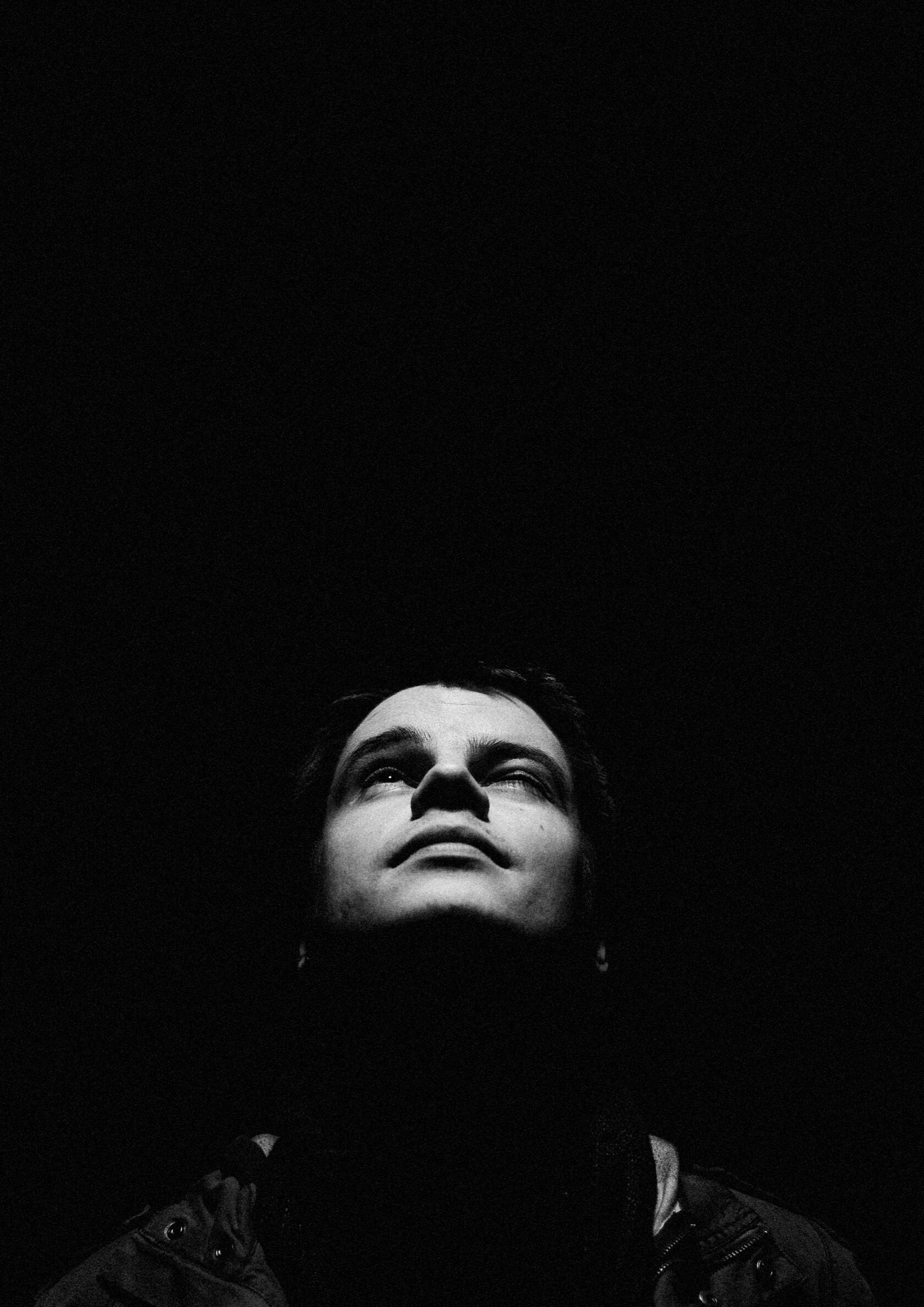 Schwarz-Weiß-Portrait eines Mannes mit Blick nach oben vor dunklem Hintergrund