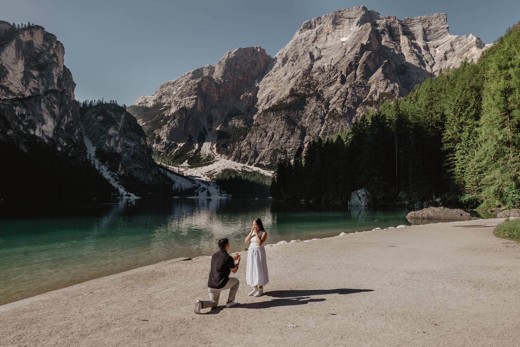 Paar sitzt am Bergsee in den Dolomiten auf einer Bank, im Hintergrund imposante Gipfel