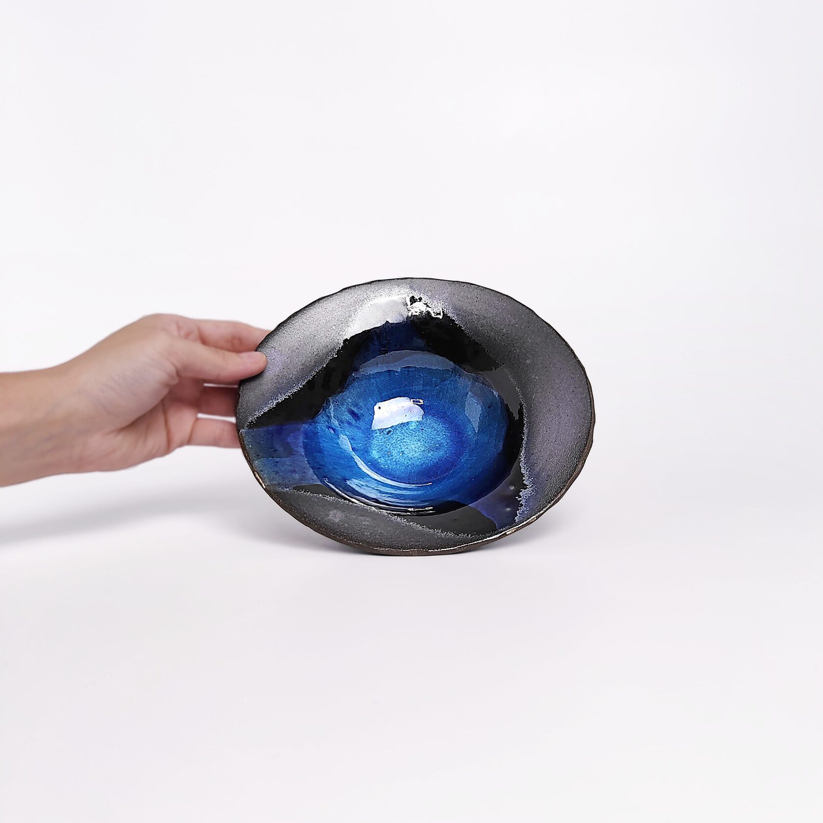 Handmade decorative ceramic plate with deep blue glossy glaze and black clay base