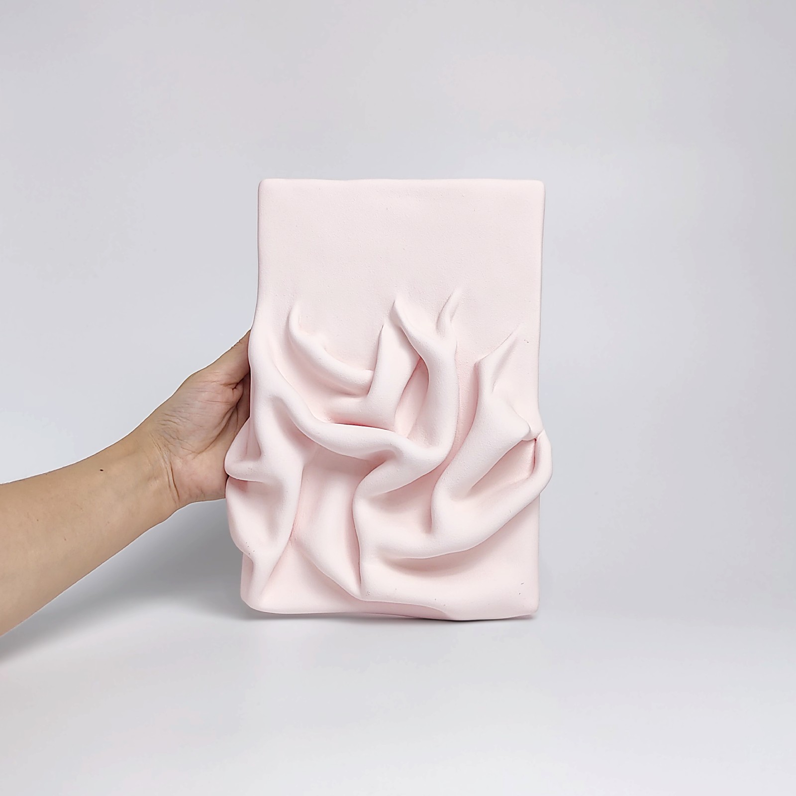 textured wall art made of air-dry clay in a soft pink shade with flowing sculpted drapery