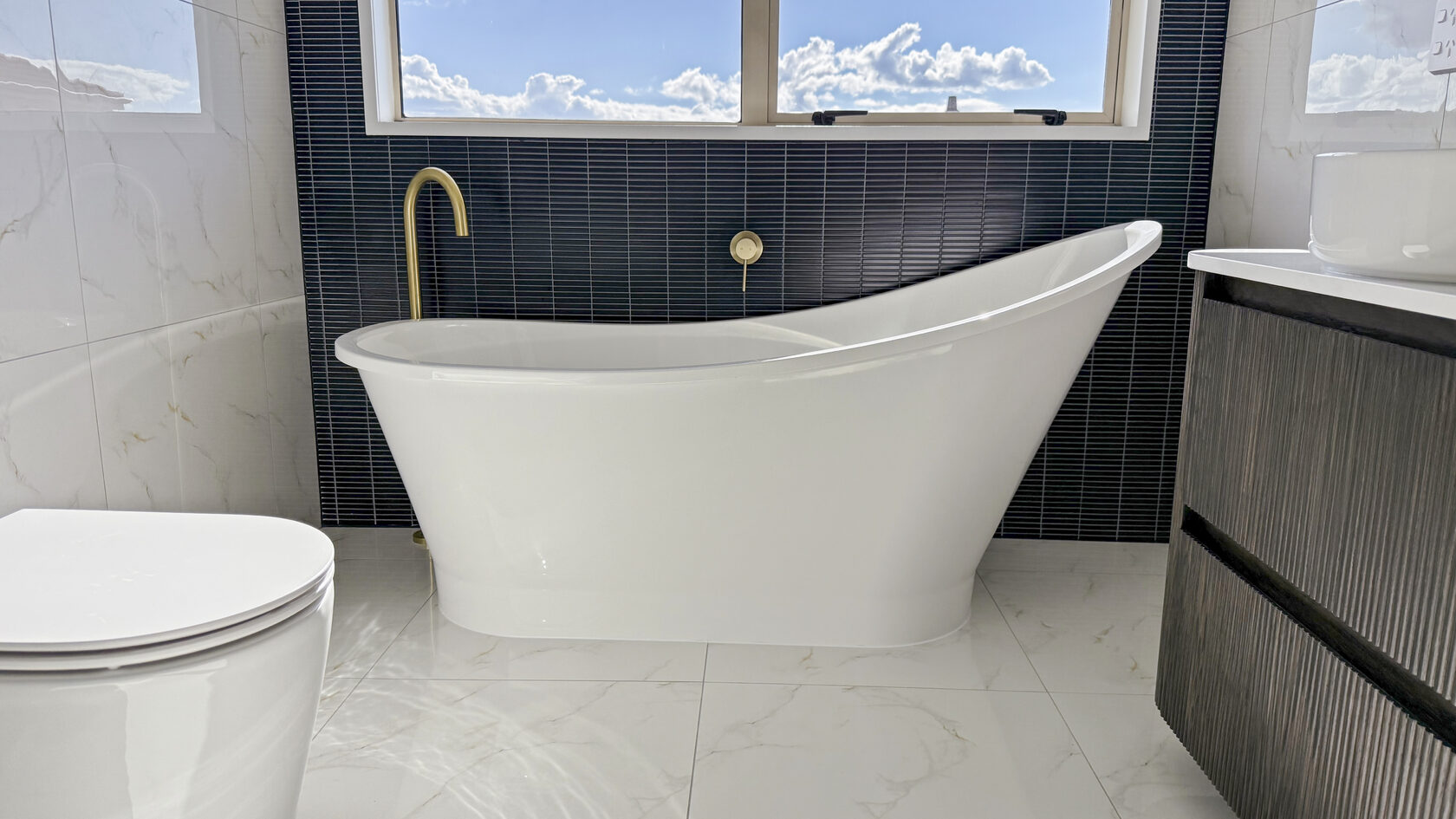 Freestanding bathtub with brass tap and black feature tiles in a St Heliers bathroom.