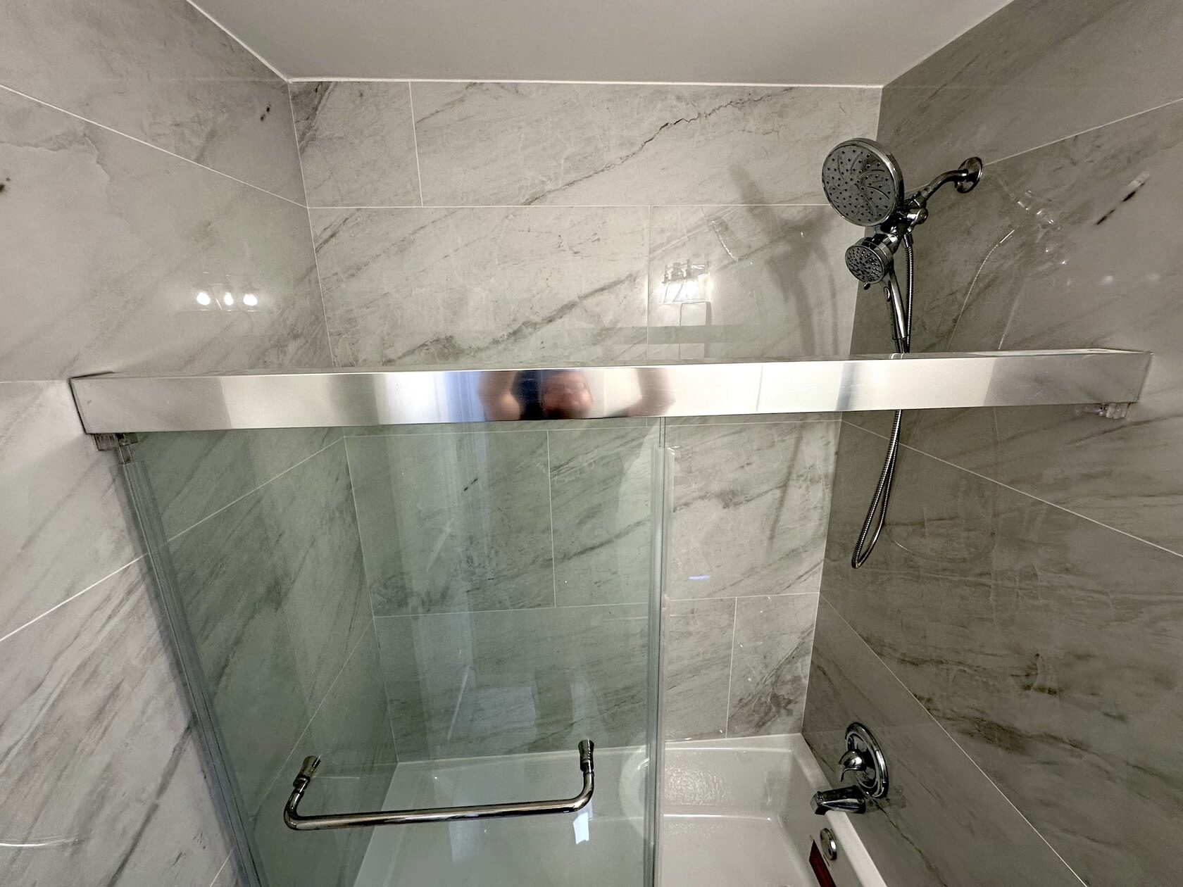 Completed Austin bathroom remodel with acrylic tub, large-format marble-look tile, glass shower panel and chrome fixtures