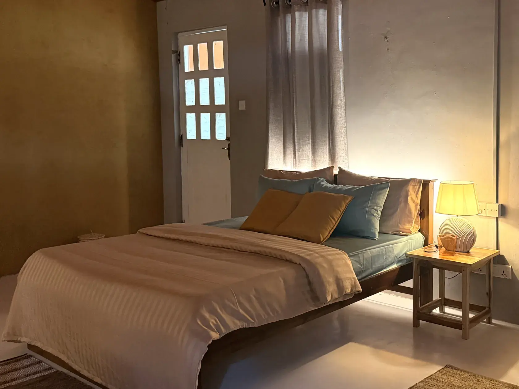 A ranch-house bedroom at Punanai in soft window light, linen bedding and a single lamp lit.