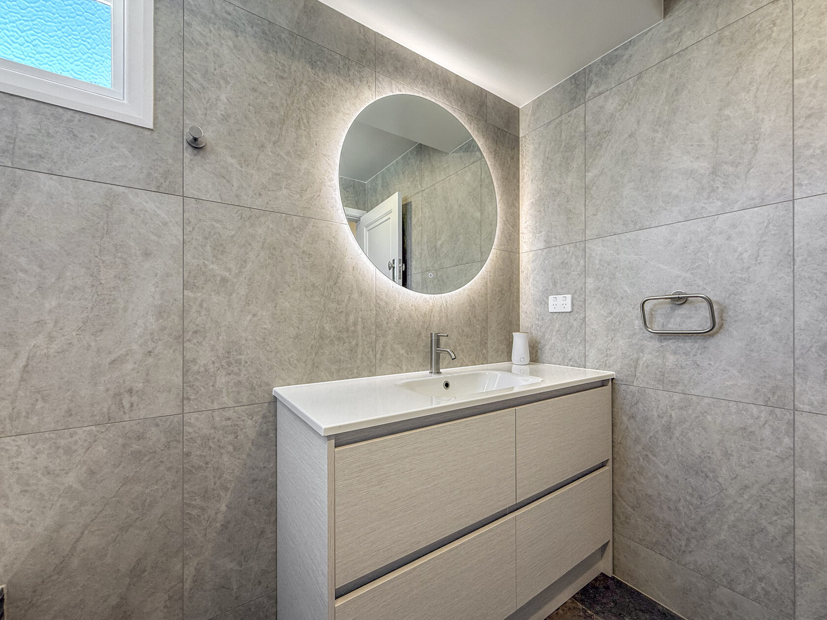 Renovated bathroom vanity beside a window and grey tiled wall