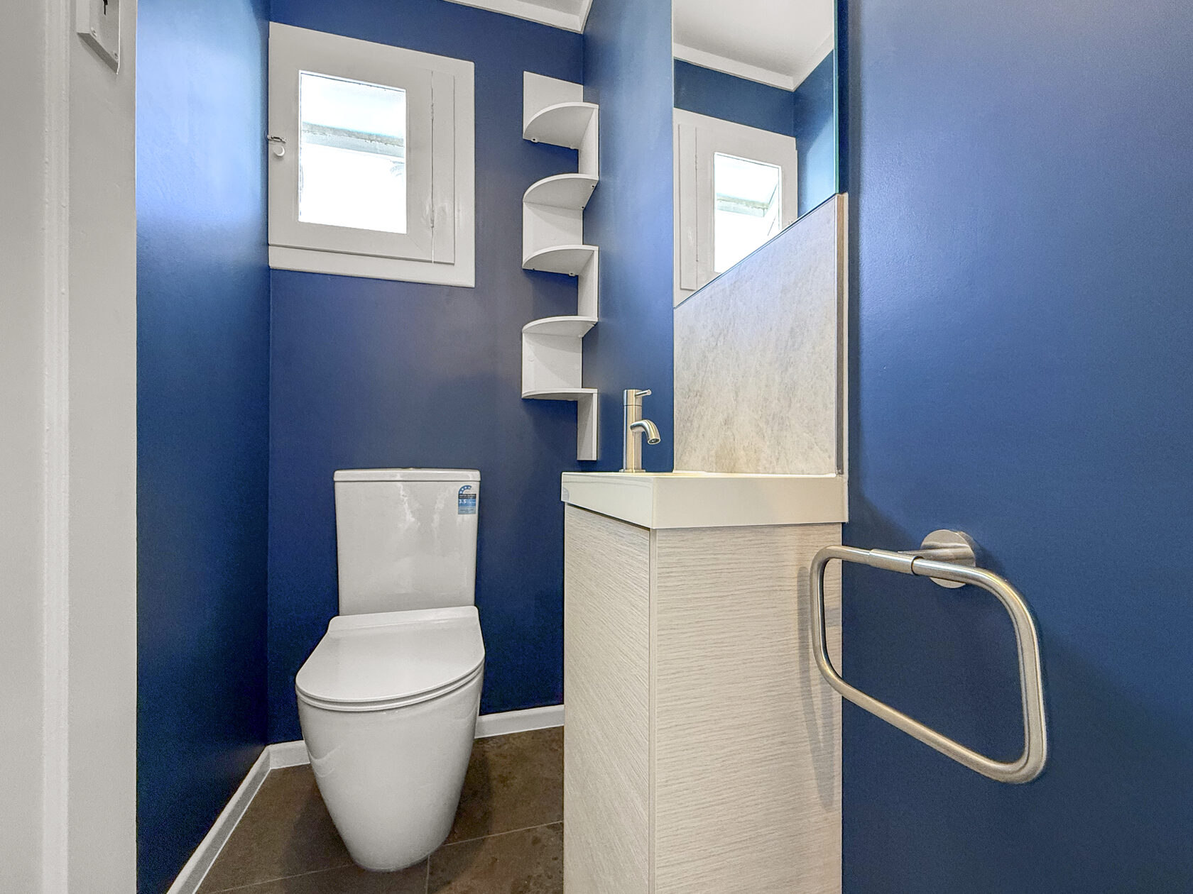 Compact toilet room with blue walls, white toilet and small vanity