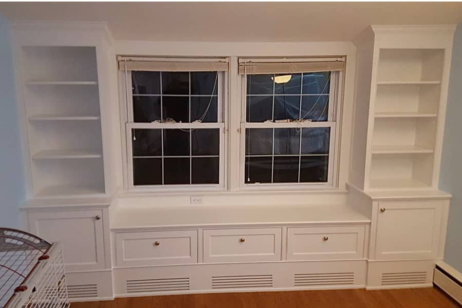 Bedroom built-in window seat in white with shelves and storage cabinets 