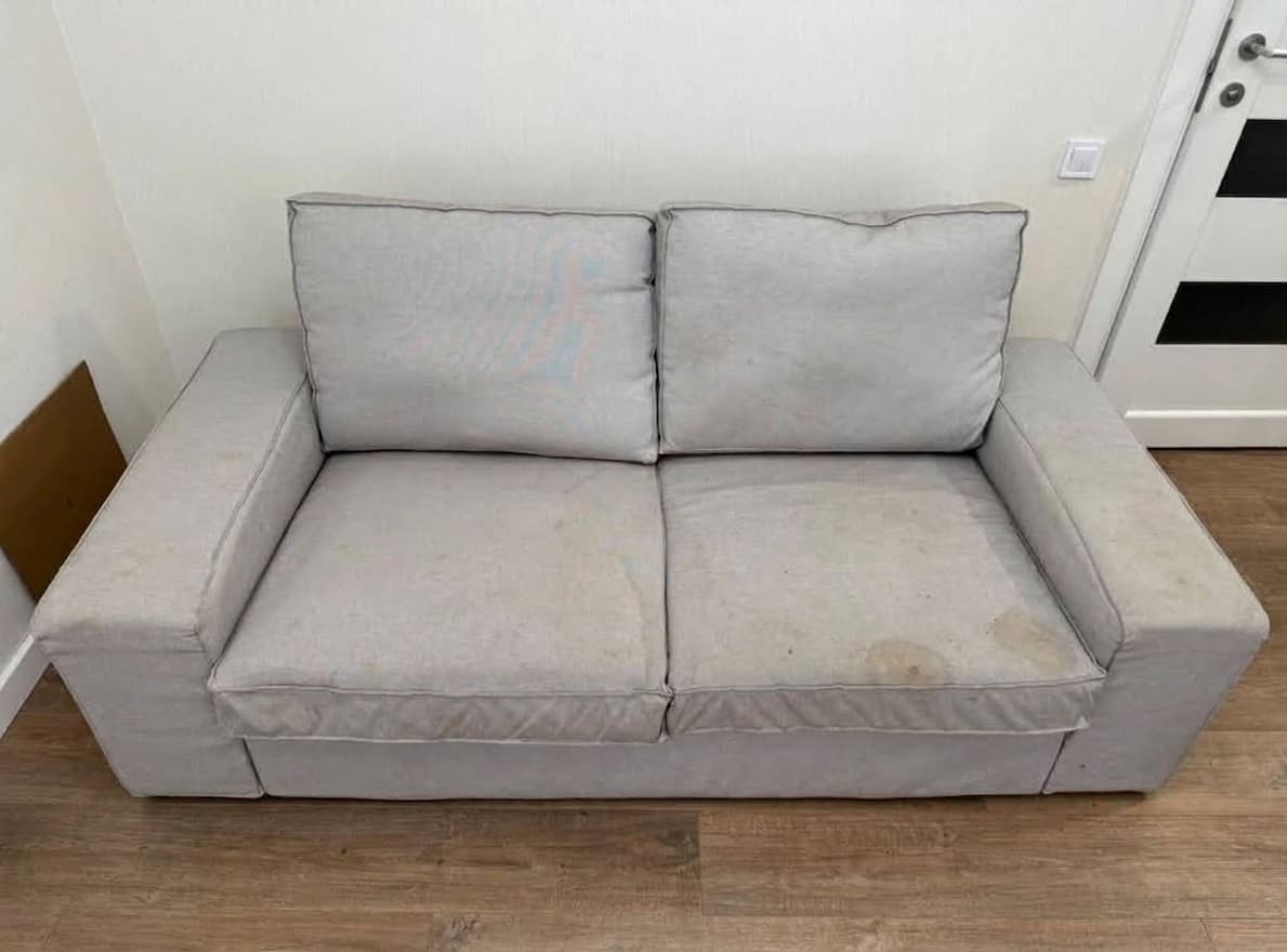 Graues Zweisitzer-Sofa aus Mikrofaser vor der professionellen Reinigung, mit dunkleren Sitzfl&auml;chen, Gebrauchsspuren und abgestandenem Geruch nach Jahren im Alltag. Der Kunde hat das Foto selbst aufgenommen und seiner Google-Bewertung f&uuml;r Shikardos Reinigung in Frankfurt beigef&uuml;gt.