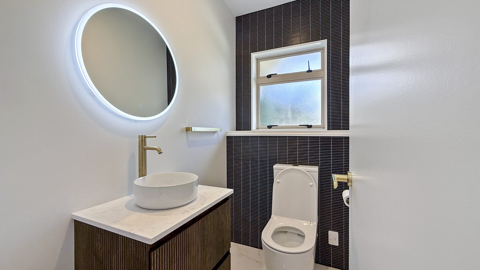 St Heliers powder room with vessel basin, illuminated round mirror and black tiles.