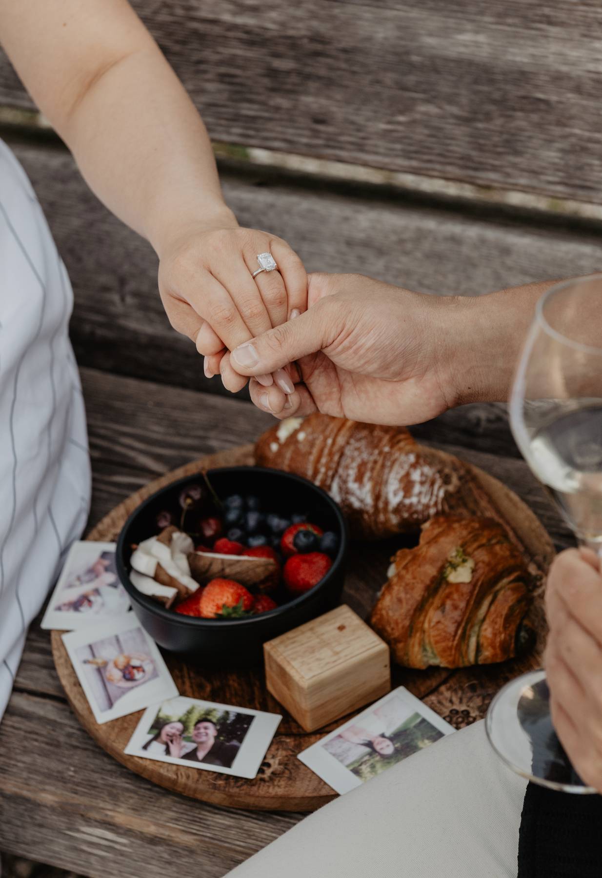 Close-up of engagement ring and hands during an alpine picnic with croissants, berries, champagne and ring box