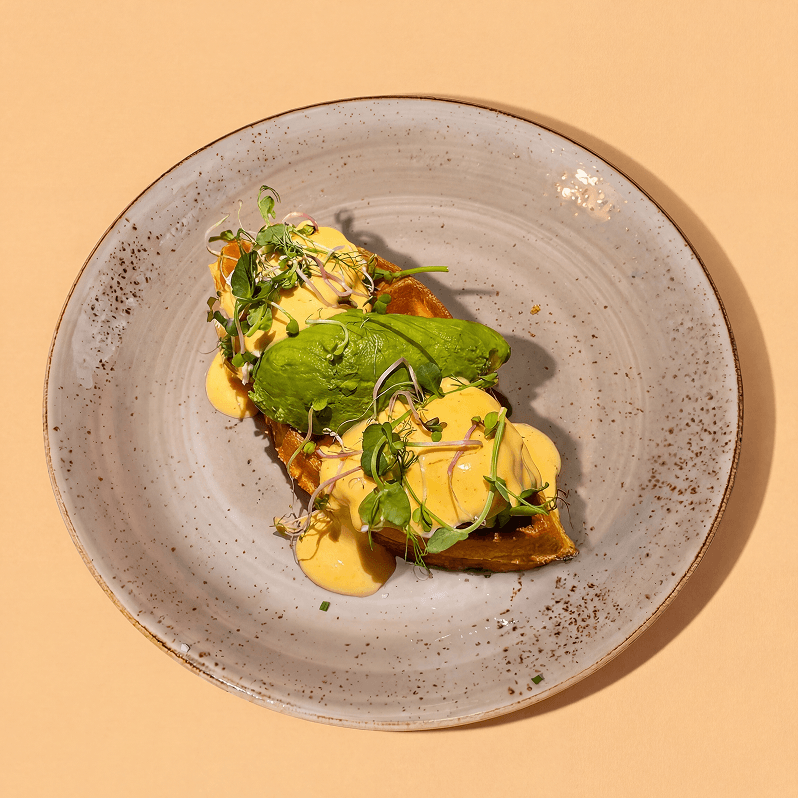 Eggs Benedict on a waffle with avocado, micro herbs and hollandaise sauce